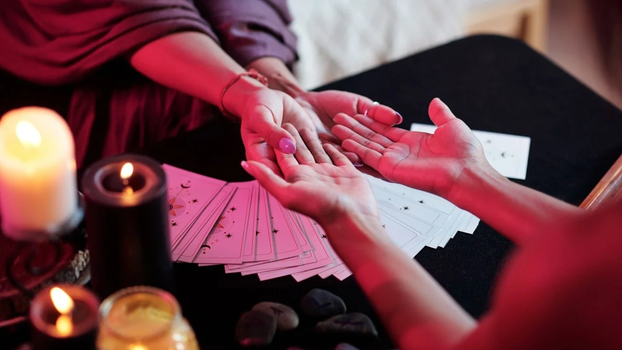 A person reading Tarot cards with another person, with lit candles on a black table.