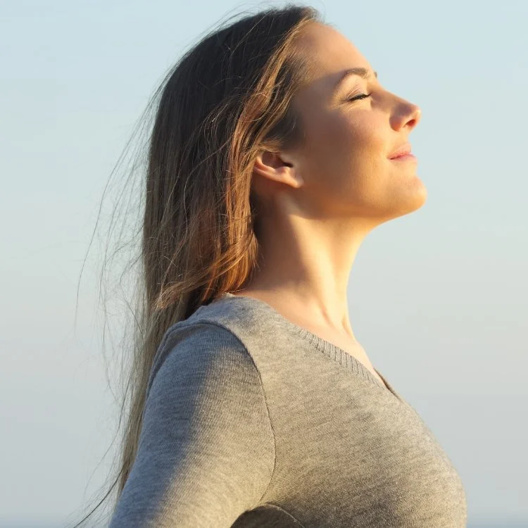 Woman with long hair enjoying sunlight with eyes closed and face tilted upwards.