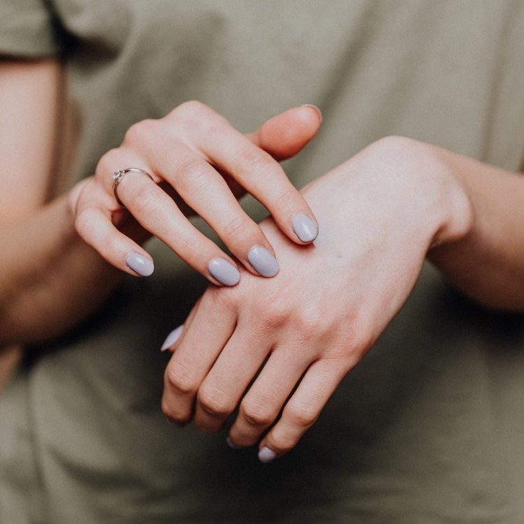 Close-up of a person's hands with light-colored nail polish, gently touching each other.