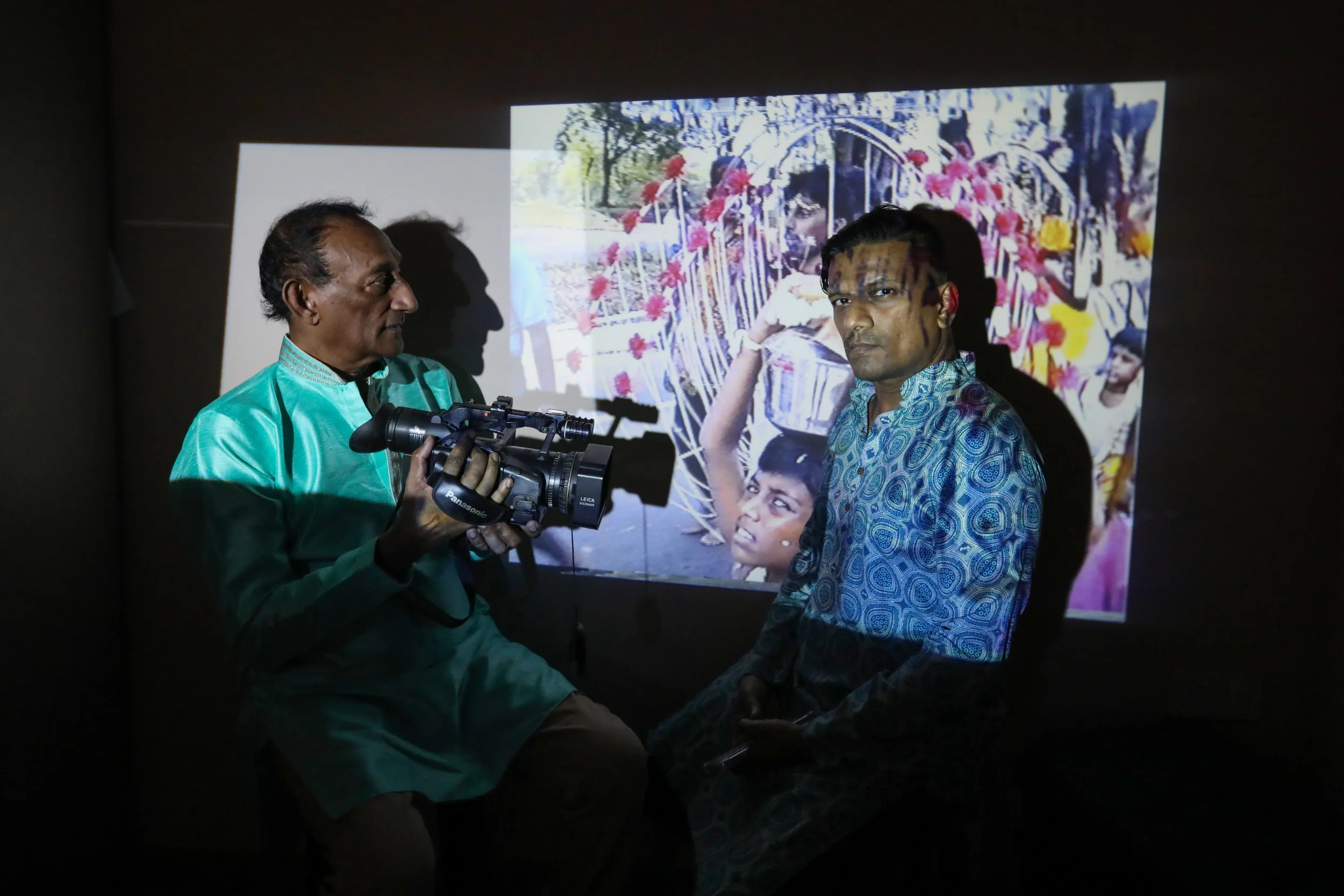 Mr S. Sathiskumar (right) standing in front of a screen showing a video recording that his father, Mr D. Sathiyanandan, captured in 1991 during Panguni Uthiram – a festival held in honour of Hindu god Murugan – when he was an 11-year-old boy carrying