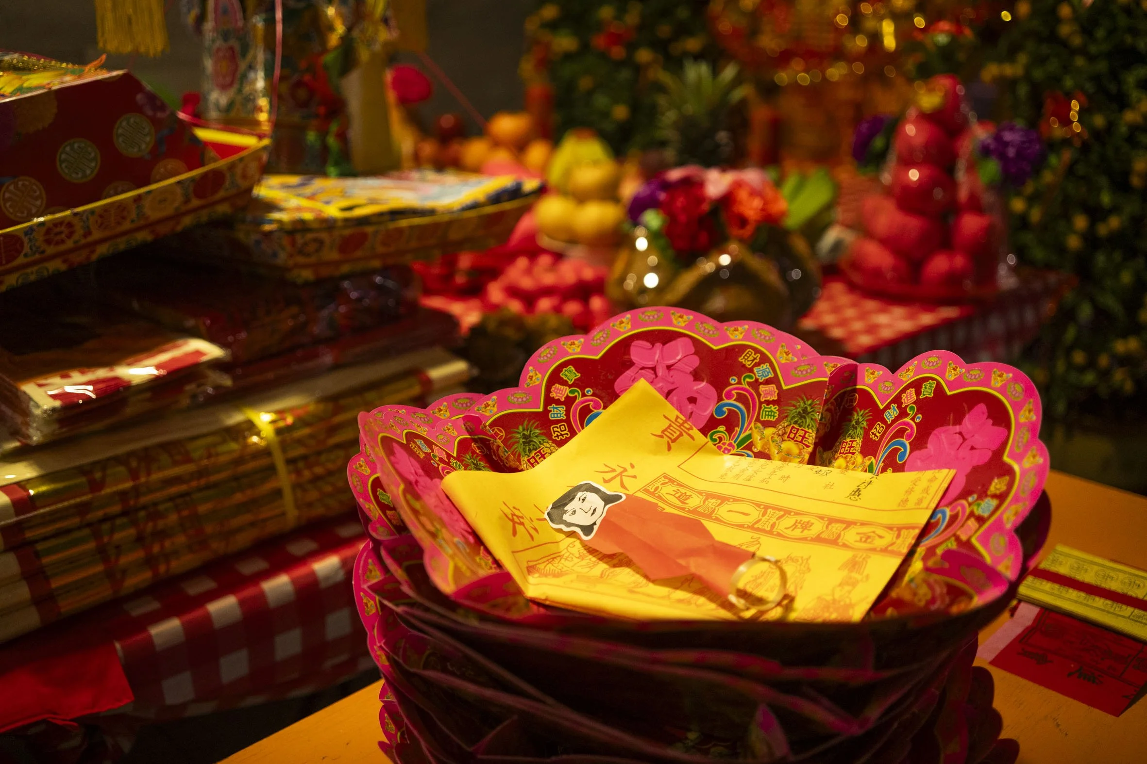 Stacked bowls of birth charts and cracked red egg shells beside the offerings table. 