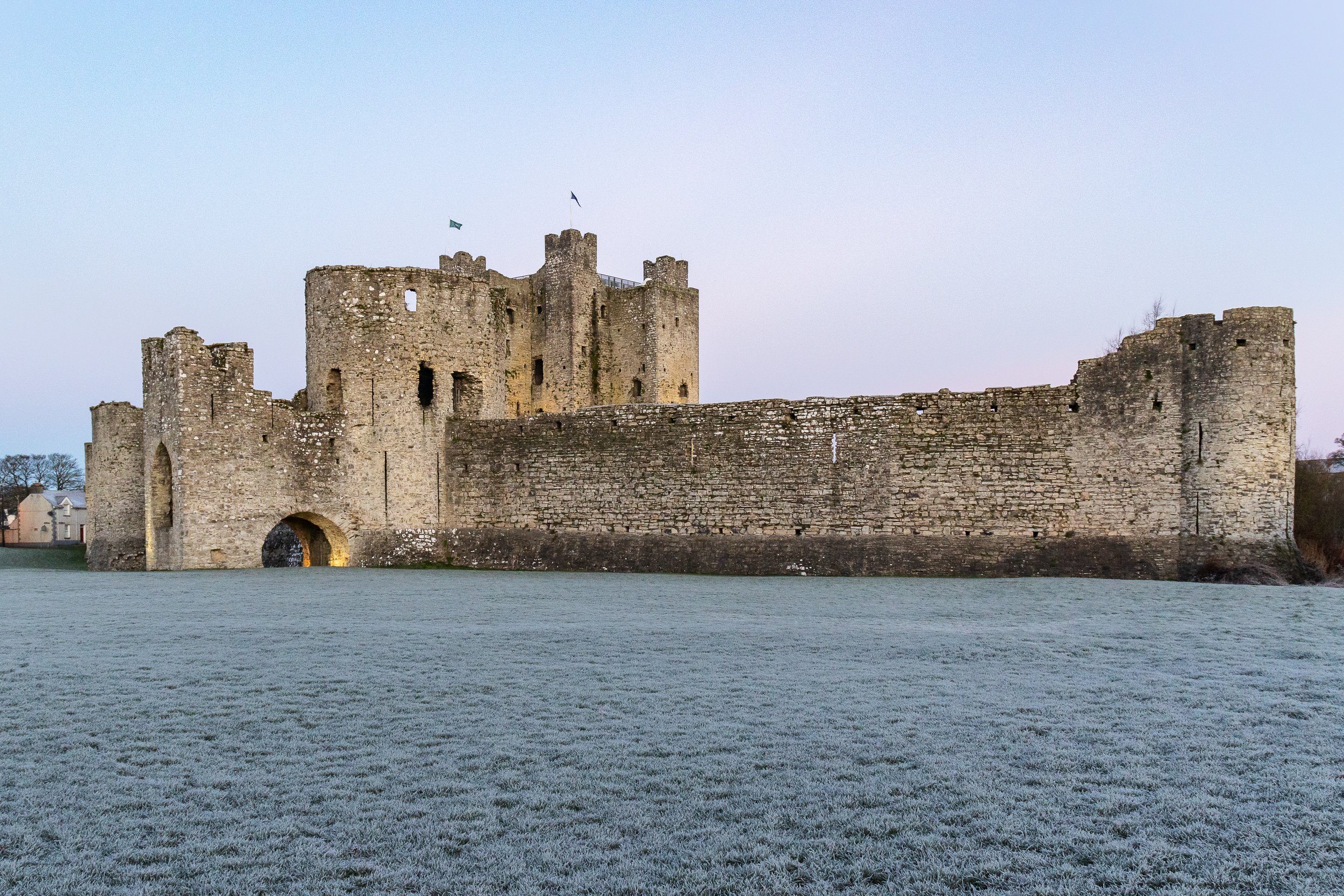 A historic stone castle surrounded by a moat, with a well-preserved tower and curtains, against a pale sky.