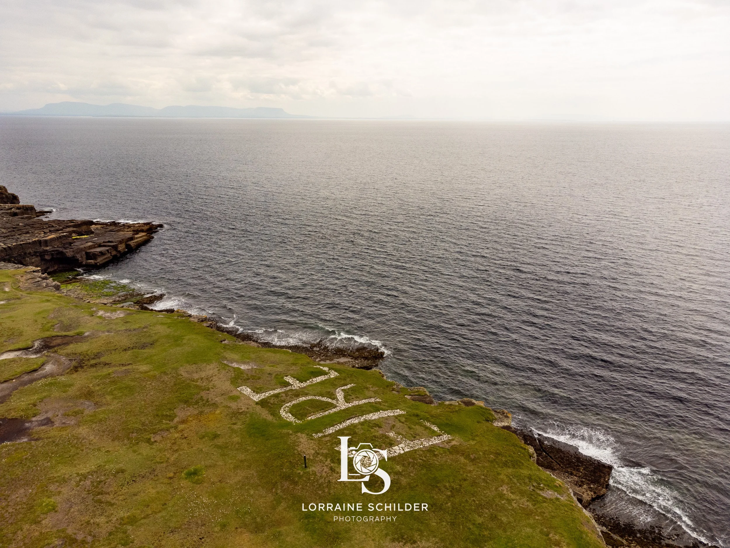A coastal landscape with grassy terrain, rocky cliffs, and the ocean extending to the horizon with distant islands or landforms.  Donegal.