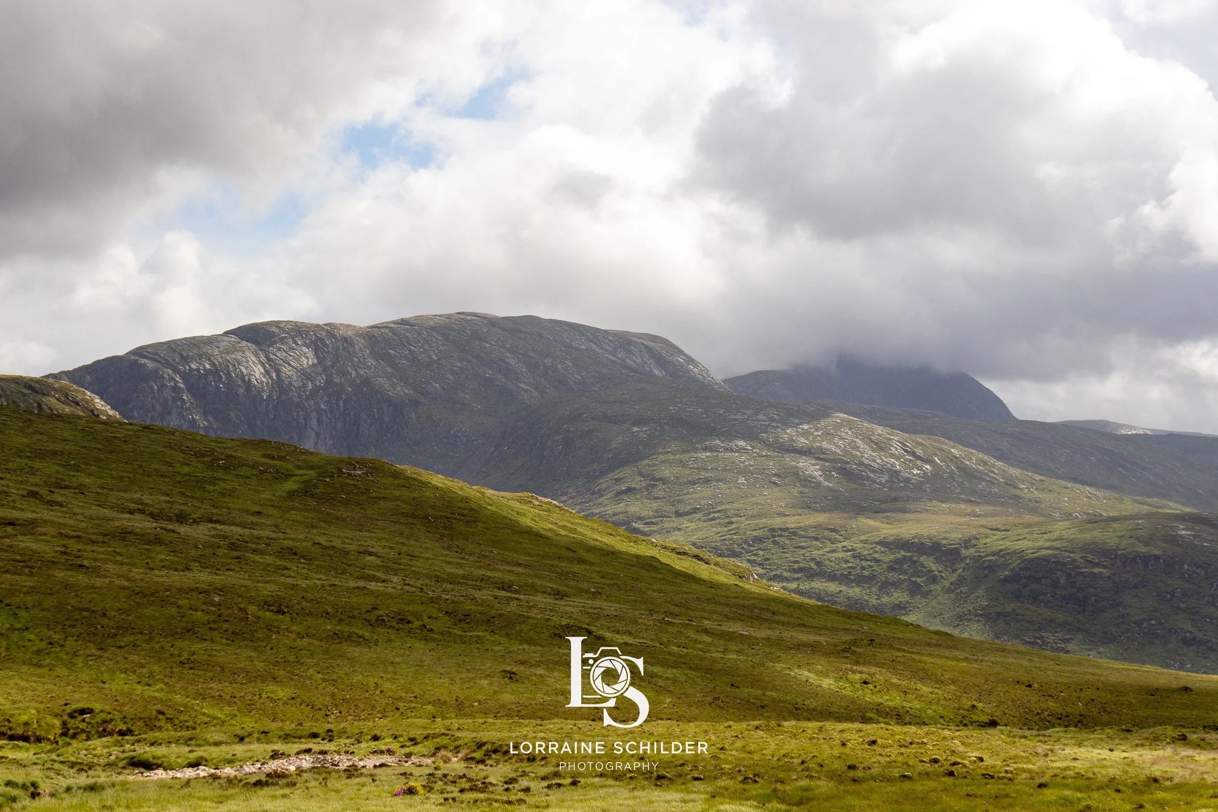 Scenic view of rolling green hills and mountains under cloudy sky.  Donegal.
