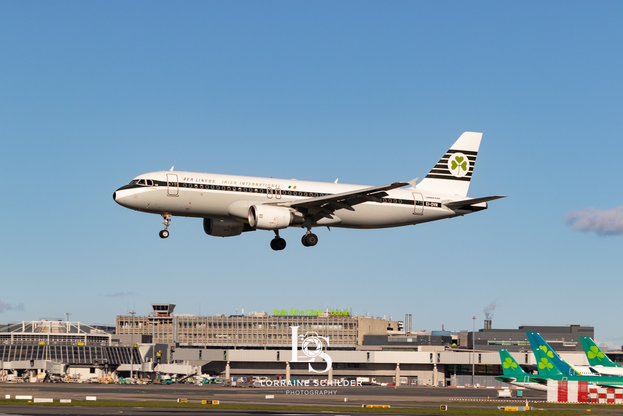 An aircraft in flight during landing at Dublin Airport, with other planes on the tarmac and airport buildings in the background. Dublin, Ireland.