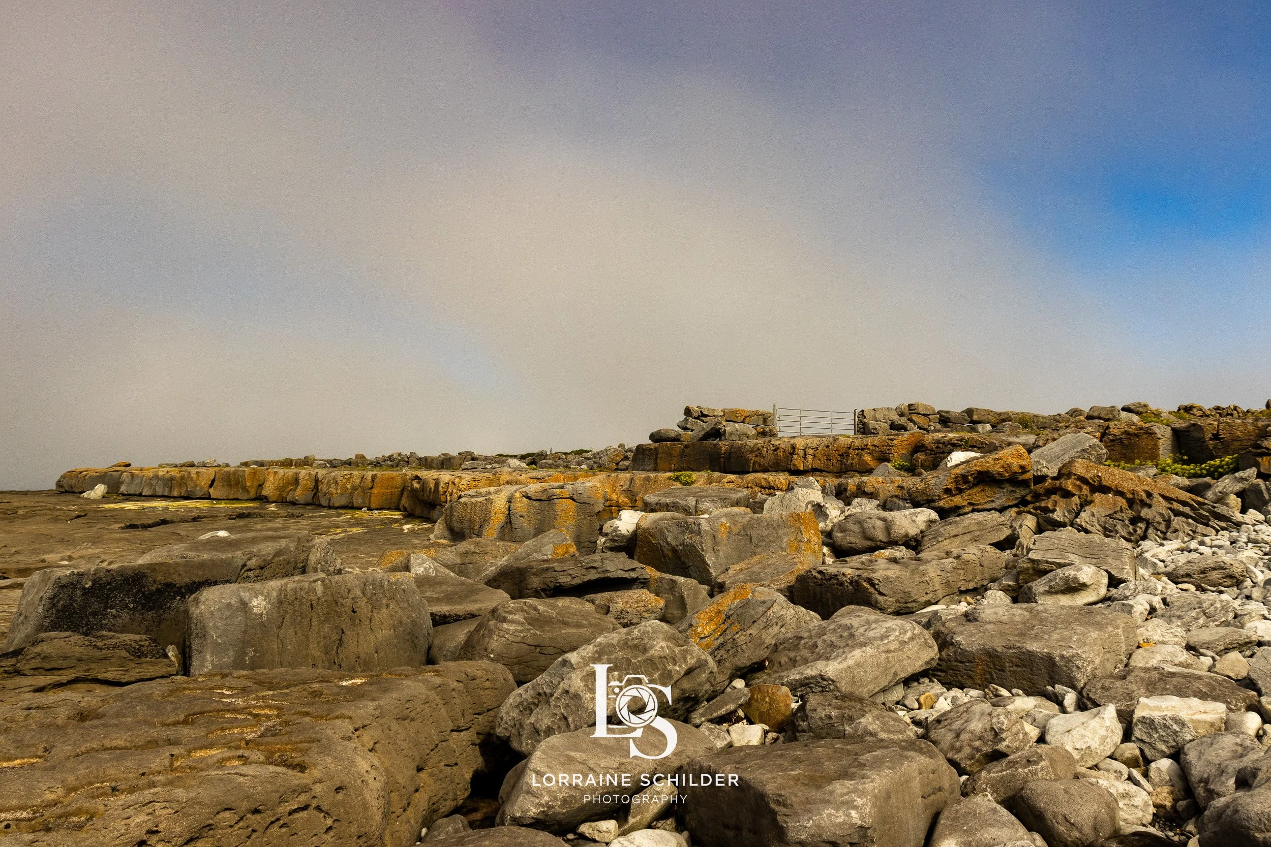 Rocky beach with large stones and a stone wall under a cloudy sky. Doolin, Clare.