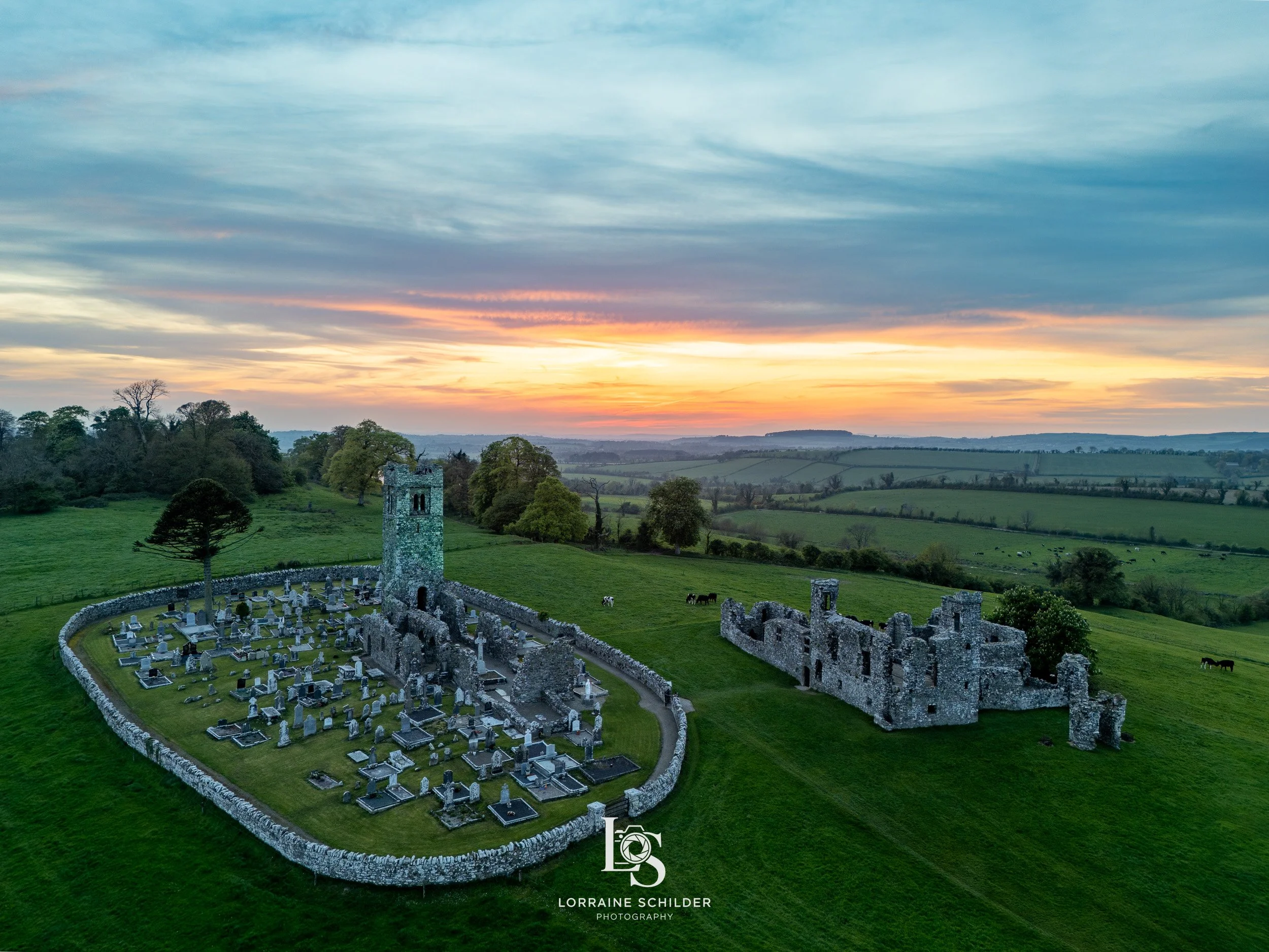 Aerial view of ancient stone church ruins and graveyard set in green fields at sunset with a colorful sky.  Slane, Meath