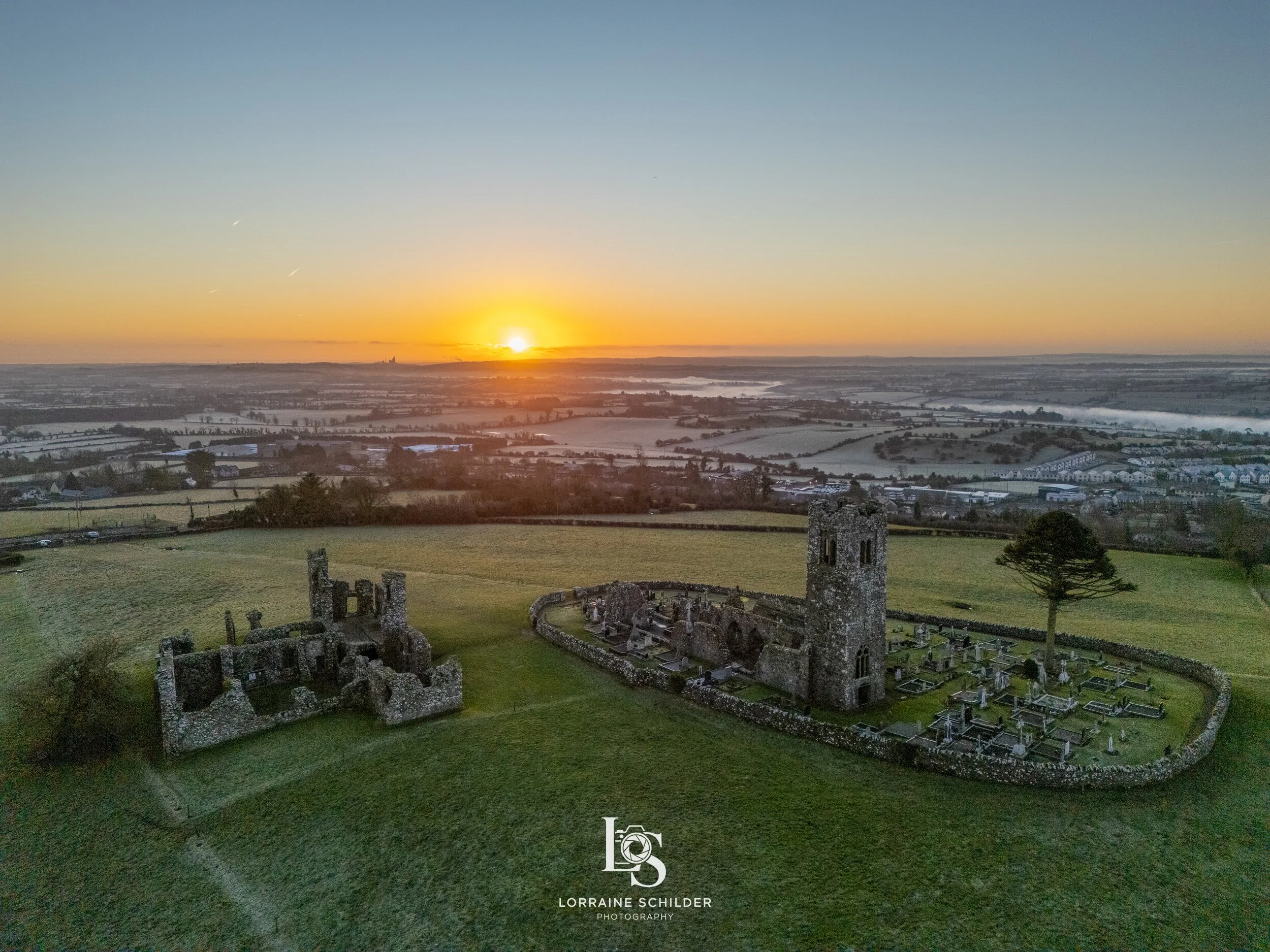 Sunrise over ruins of an ancient stone church with surrounding graveyard, rolling fields, and distant horizon.  Slane, Meath