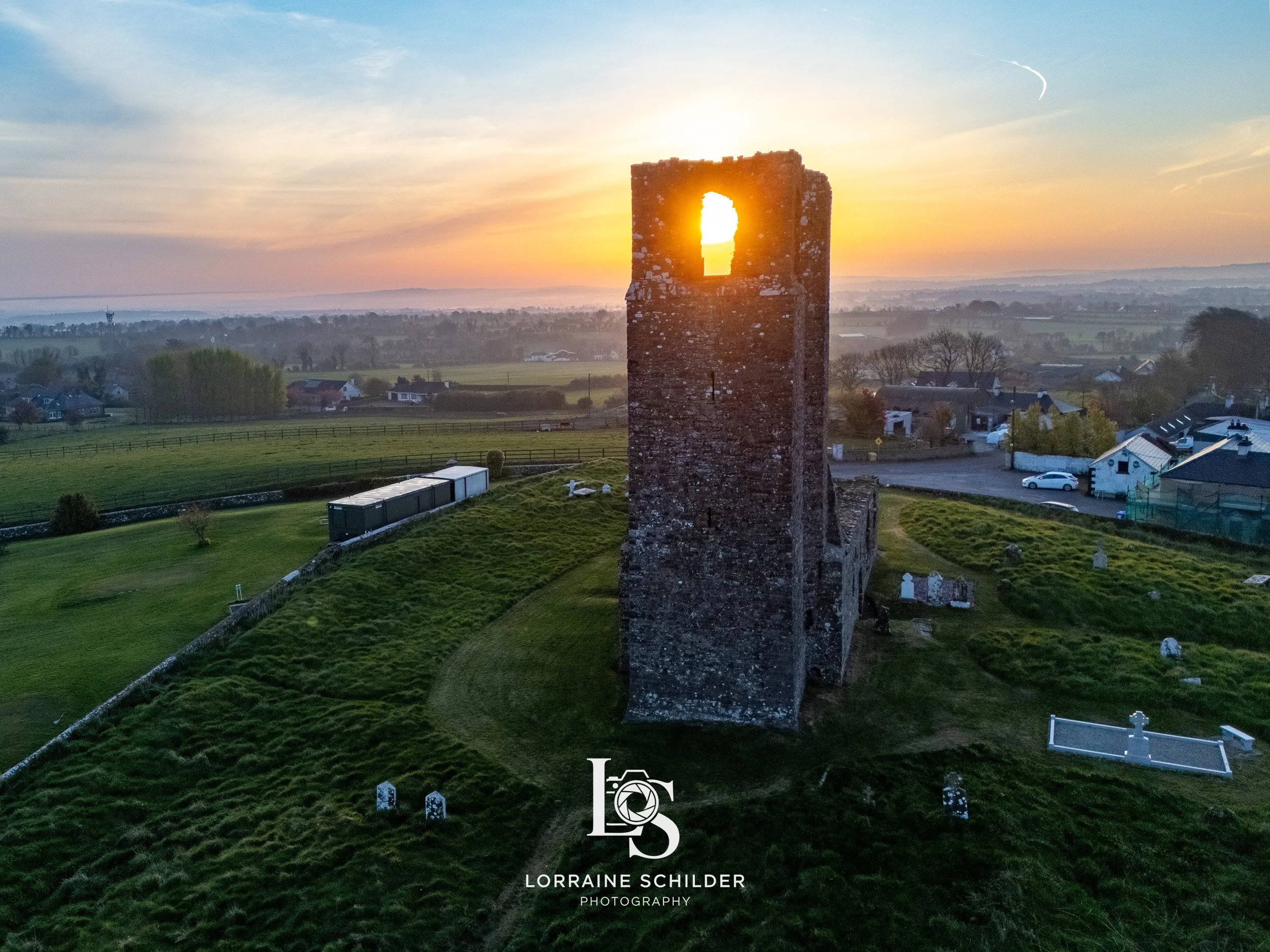 A historic stone tower with a window at sunset, overlooking a green landscape with scattered houses and trees. Skyrne, Meath.
