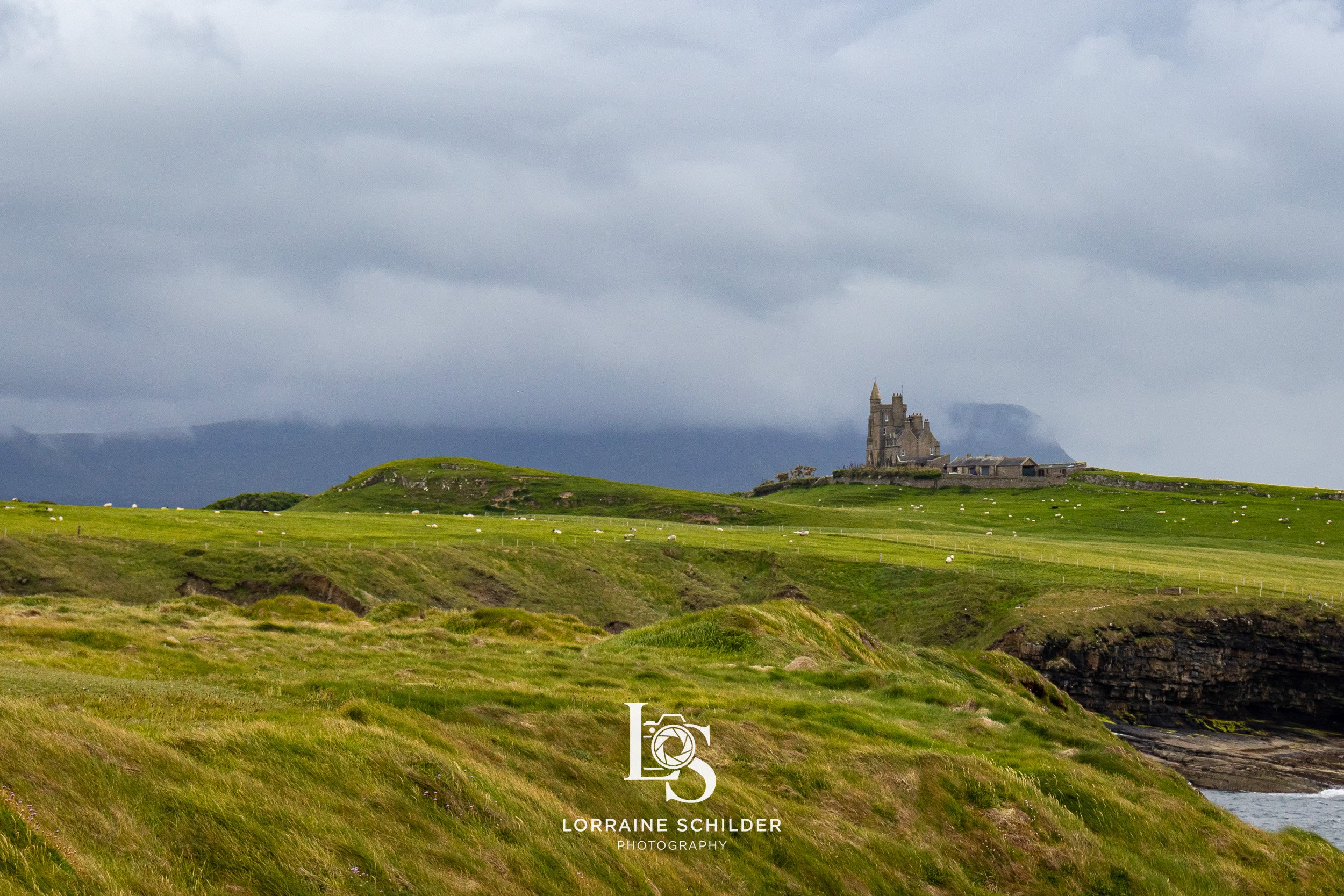 Sligo landscape with green rolling hills, an old castle in the distance, and a cloudy sky overhead. Sligo.