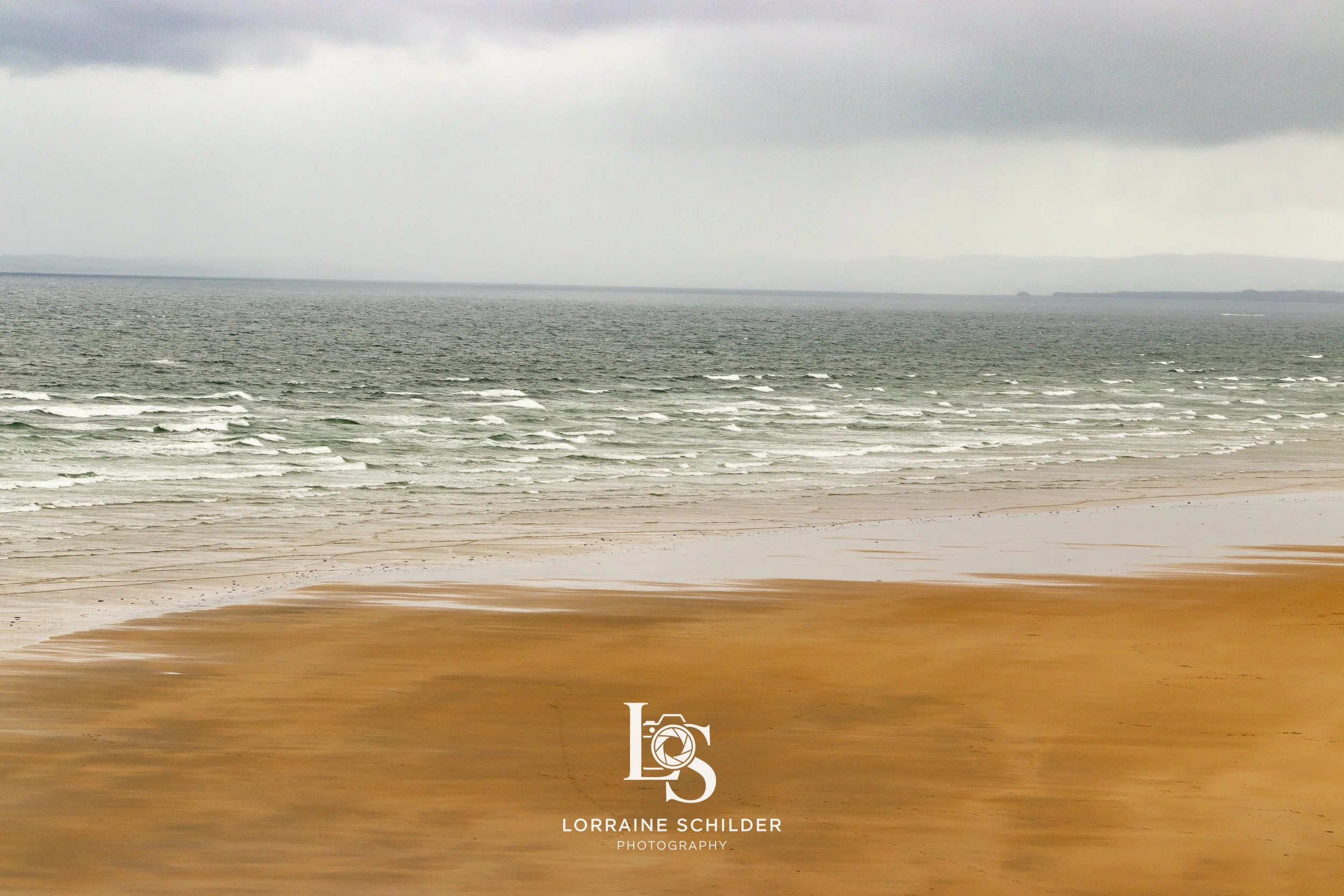 Overcast sky over a sandy beach with calm ocean waves. Sligo.