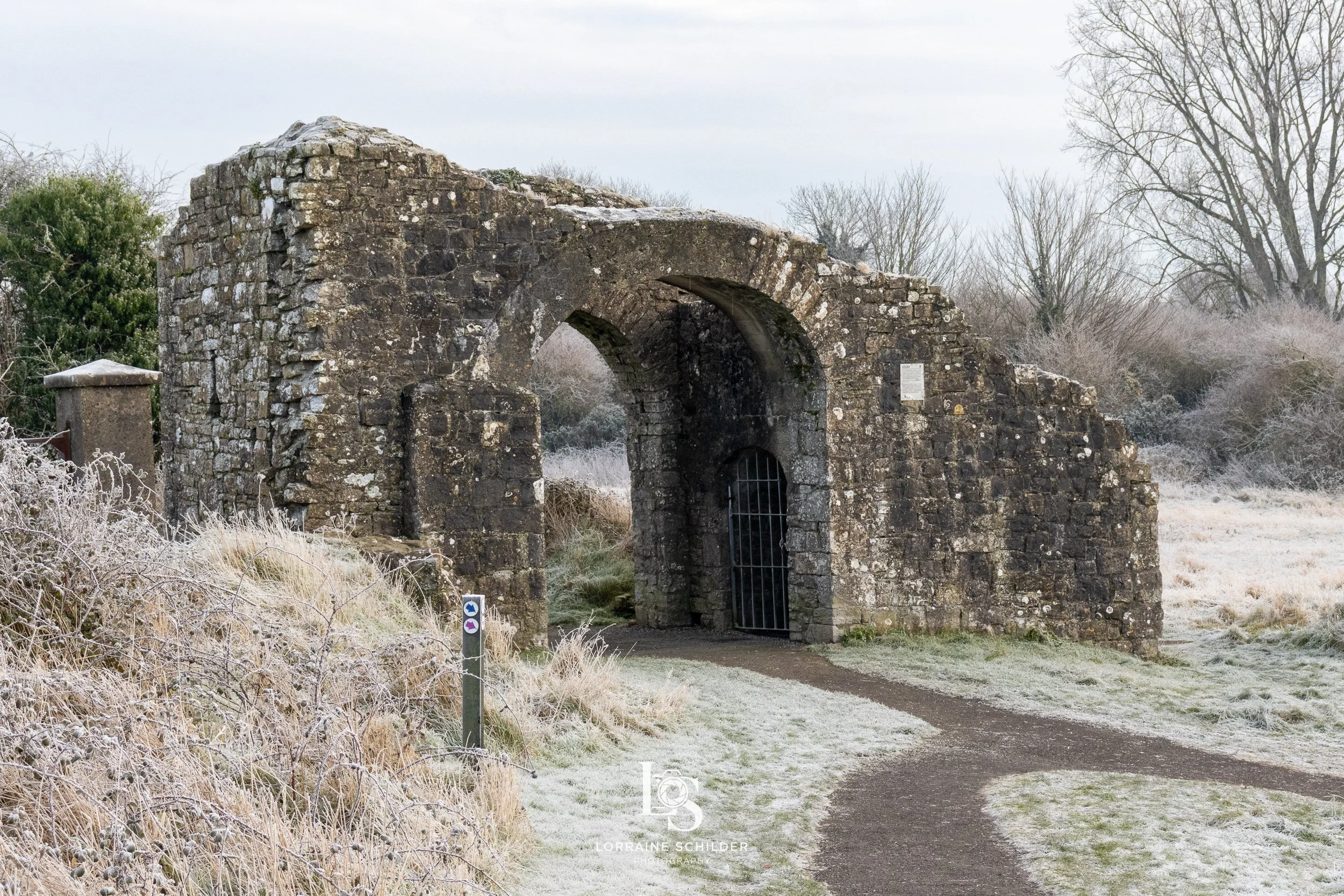The Sheep's Gate with the path leading through it, surrounded by frost-covered grass and trees in winter.