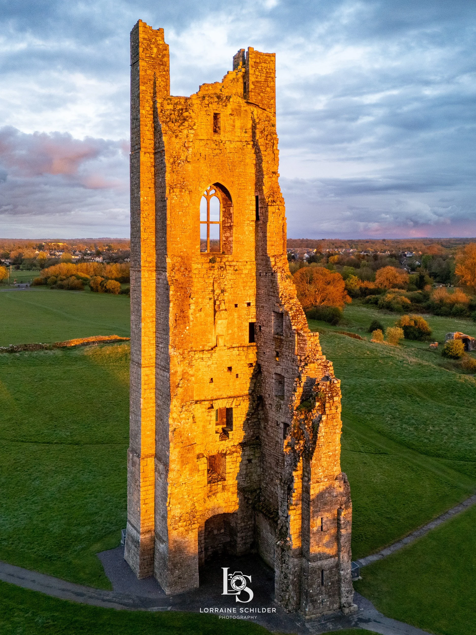 Sunlit medieval stone tower ruins in a rural landscape at sunset.