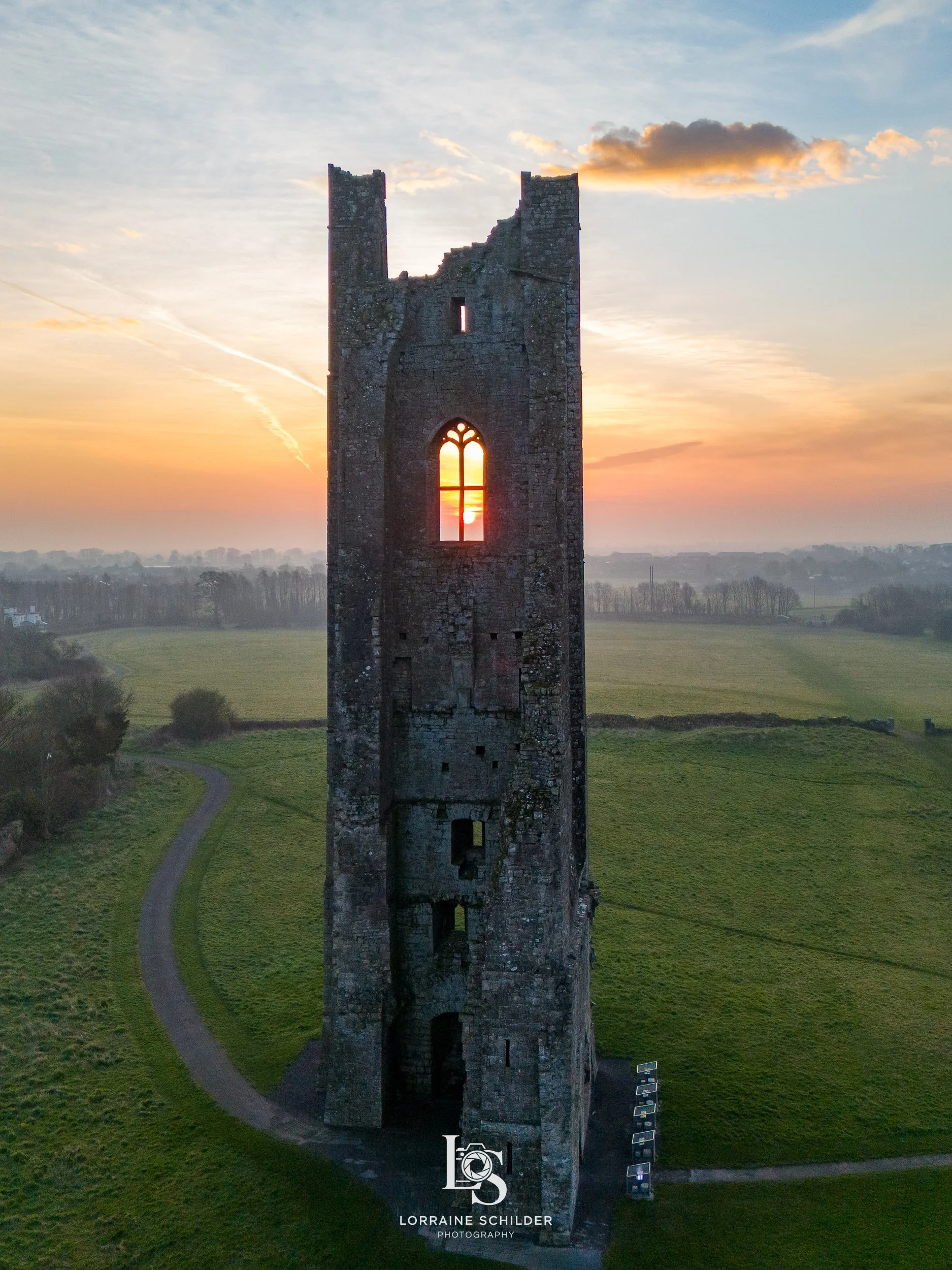 Sunset view through the window of an ancient, crumbling stone tower situated in a green landscape.
