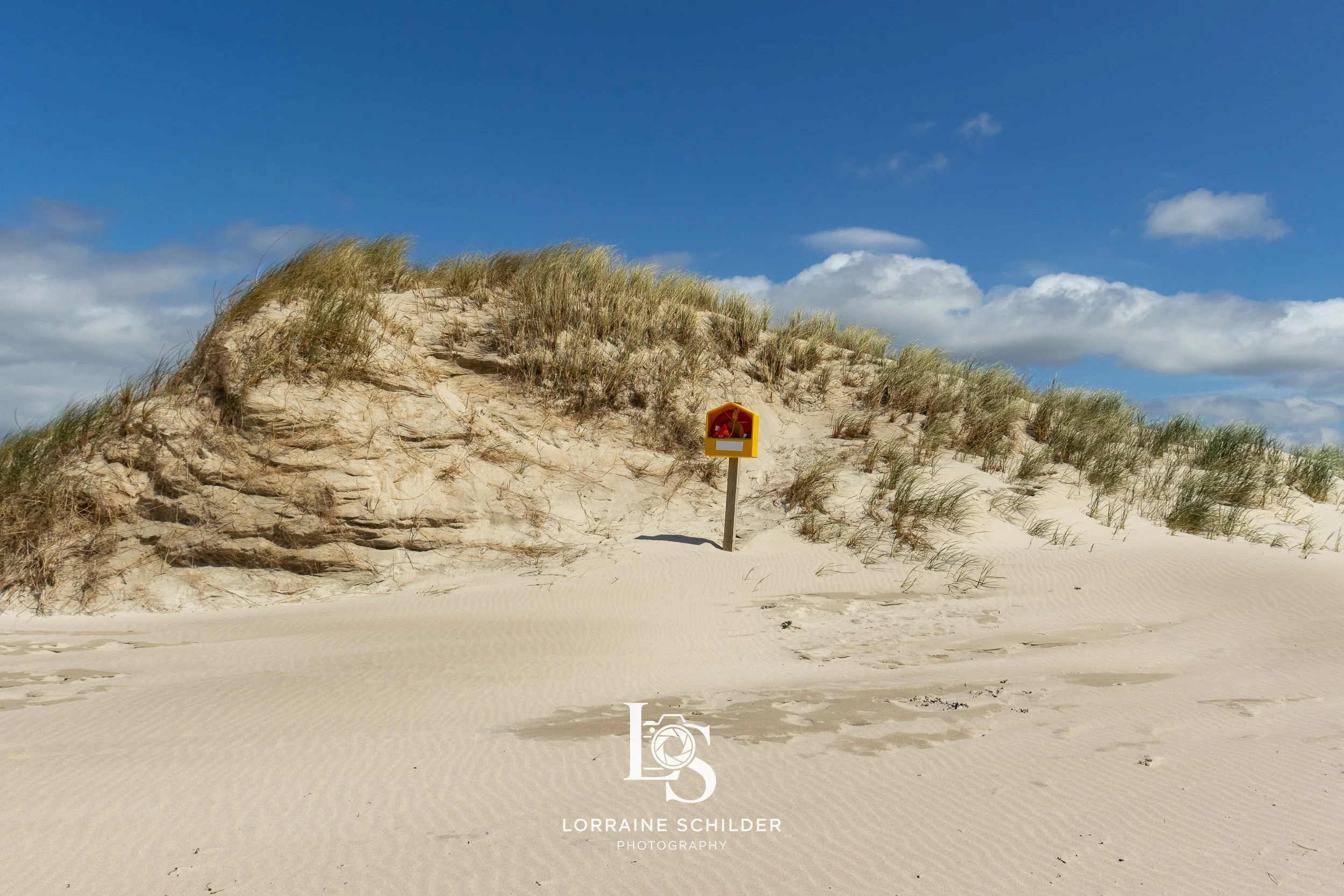 Sand dune with grass and a yellow warning sign in the middle, under a blue sky with scattered clouds.  Donegal.