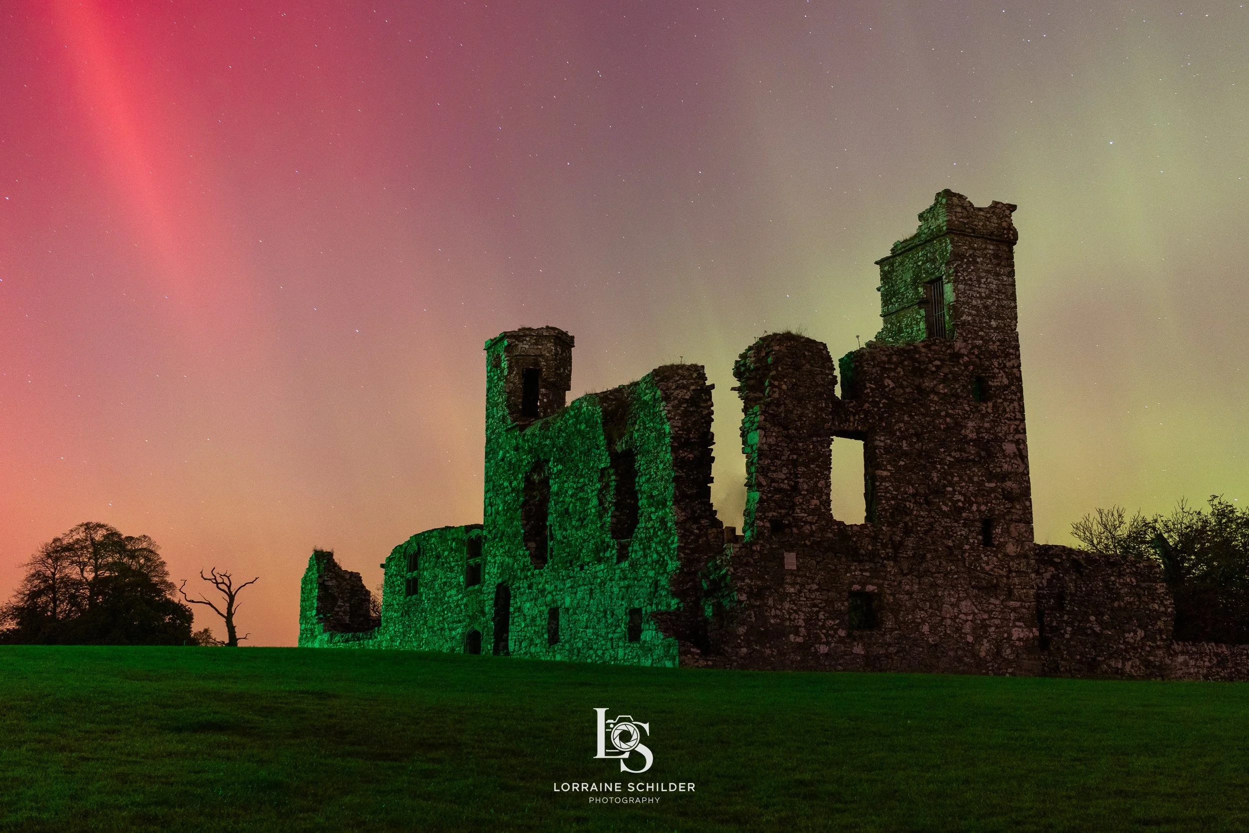 Old stone castle ruins illuminated with green lights under a starry sky with pink, green, and purple hues.  Slane, Meath