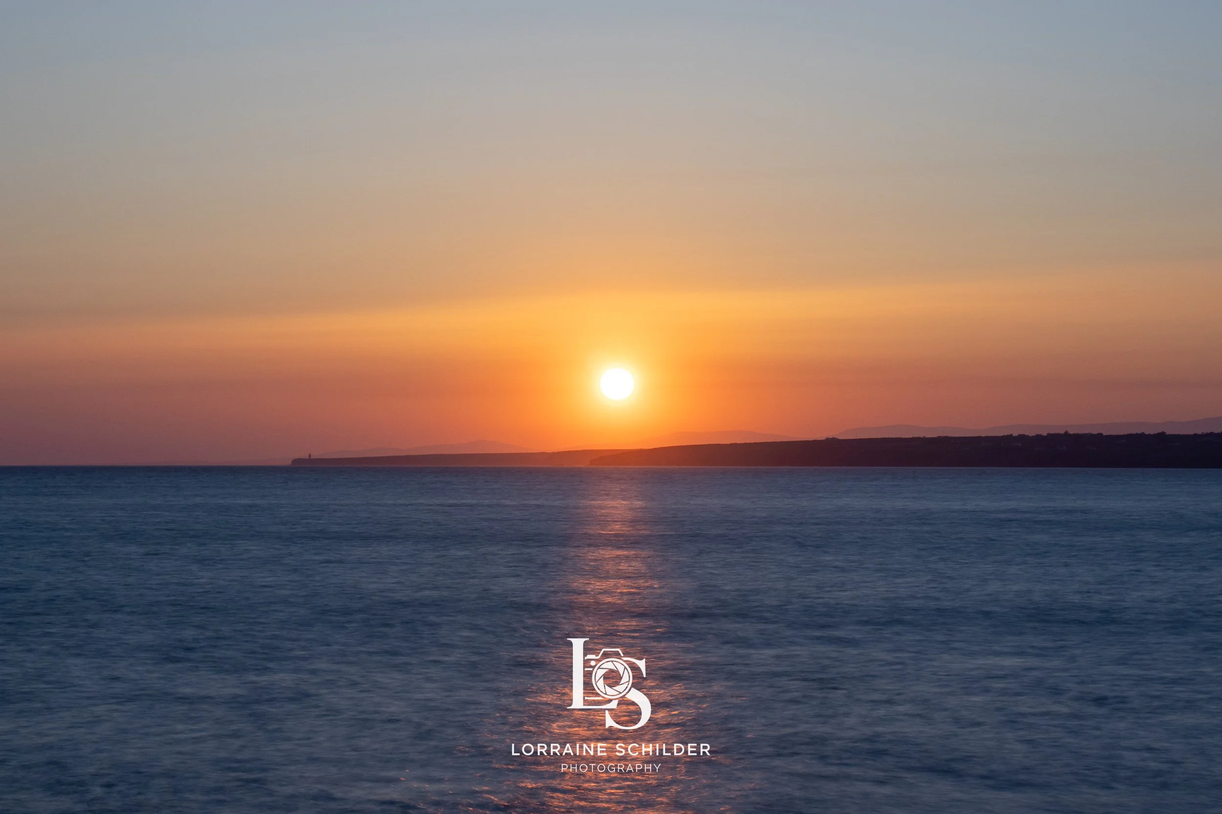 Sunset over the ocean with a silhouette of land in the distance. Wexford.