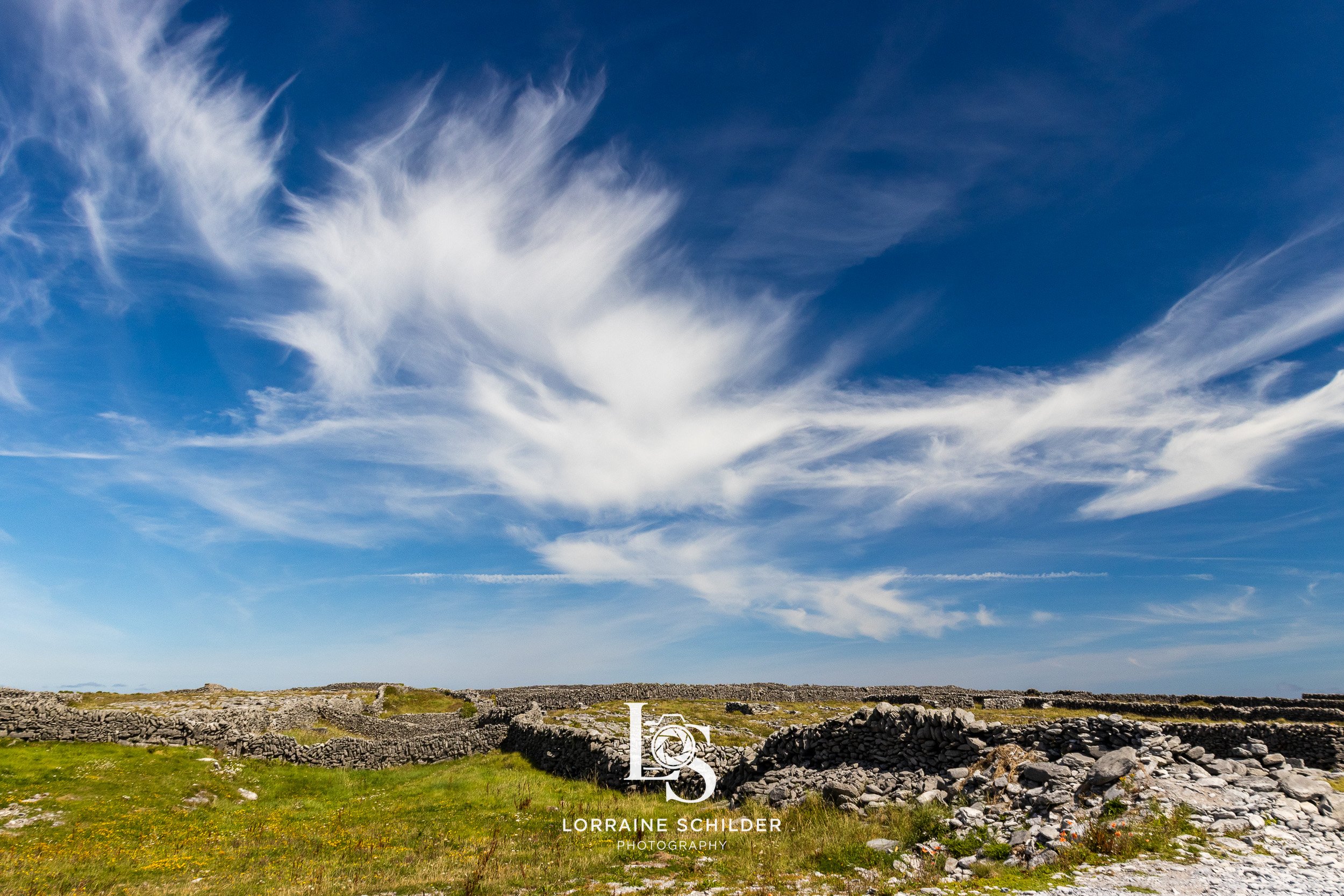 Open field with stone ruins under a blue sky with wispy white clouds.  Inisheer, Galway.