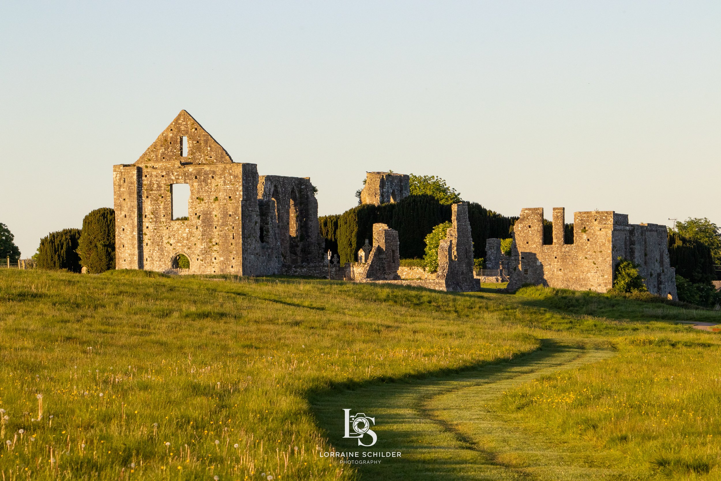 Sunlit view  Newtown ruins on a grassy hill with a grass path.