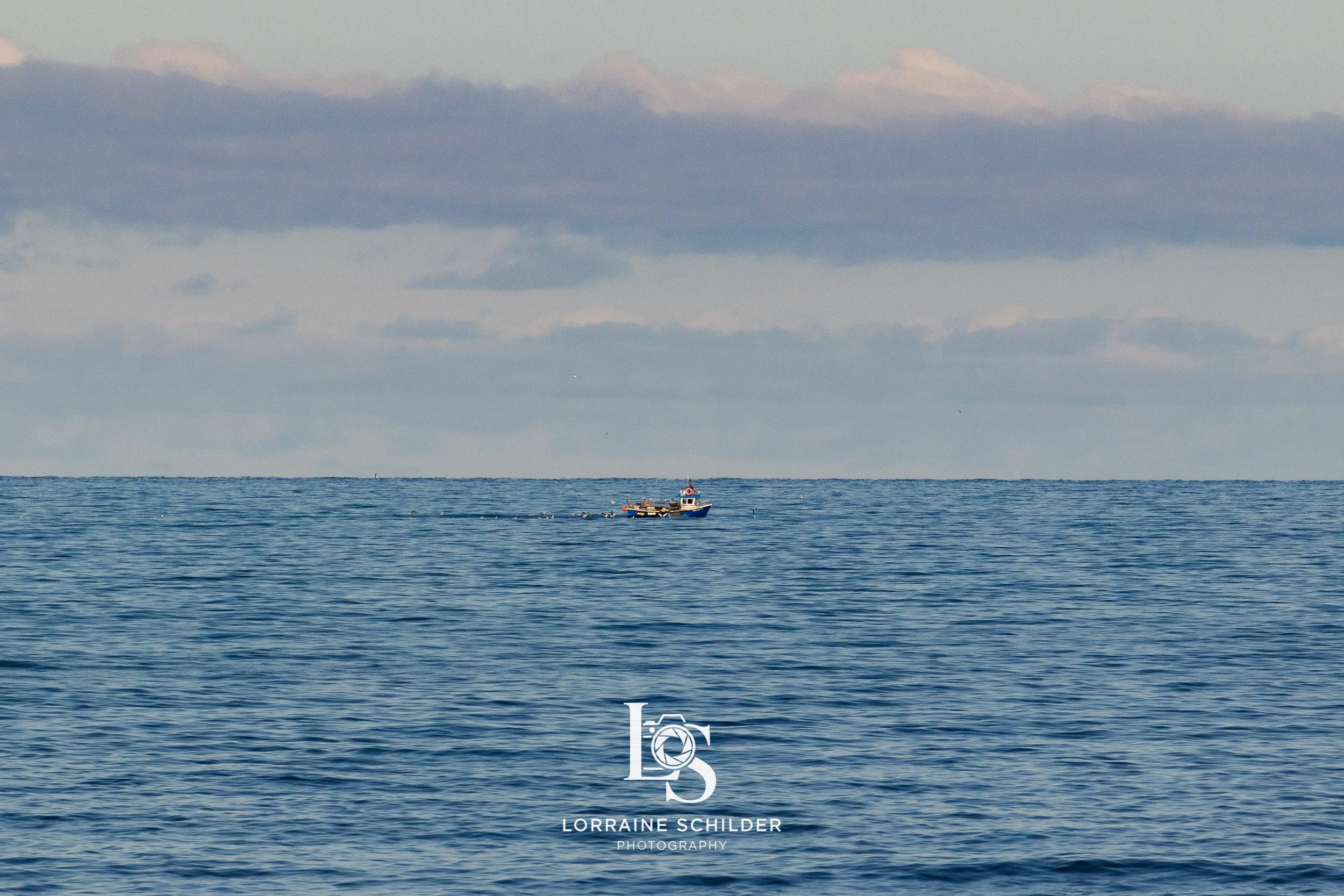A small boat sailing on the calm ocean with a cloudy sky overhead. Sligo.