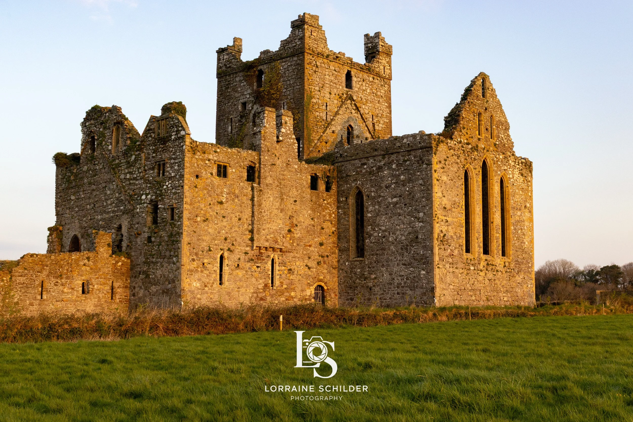 An old stone castle on a grassy field, with many windows and towers, during sunset. Wexford.