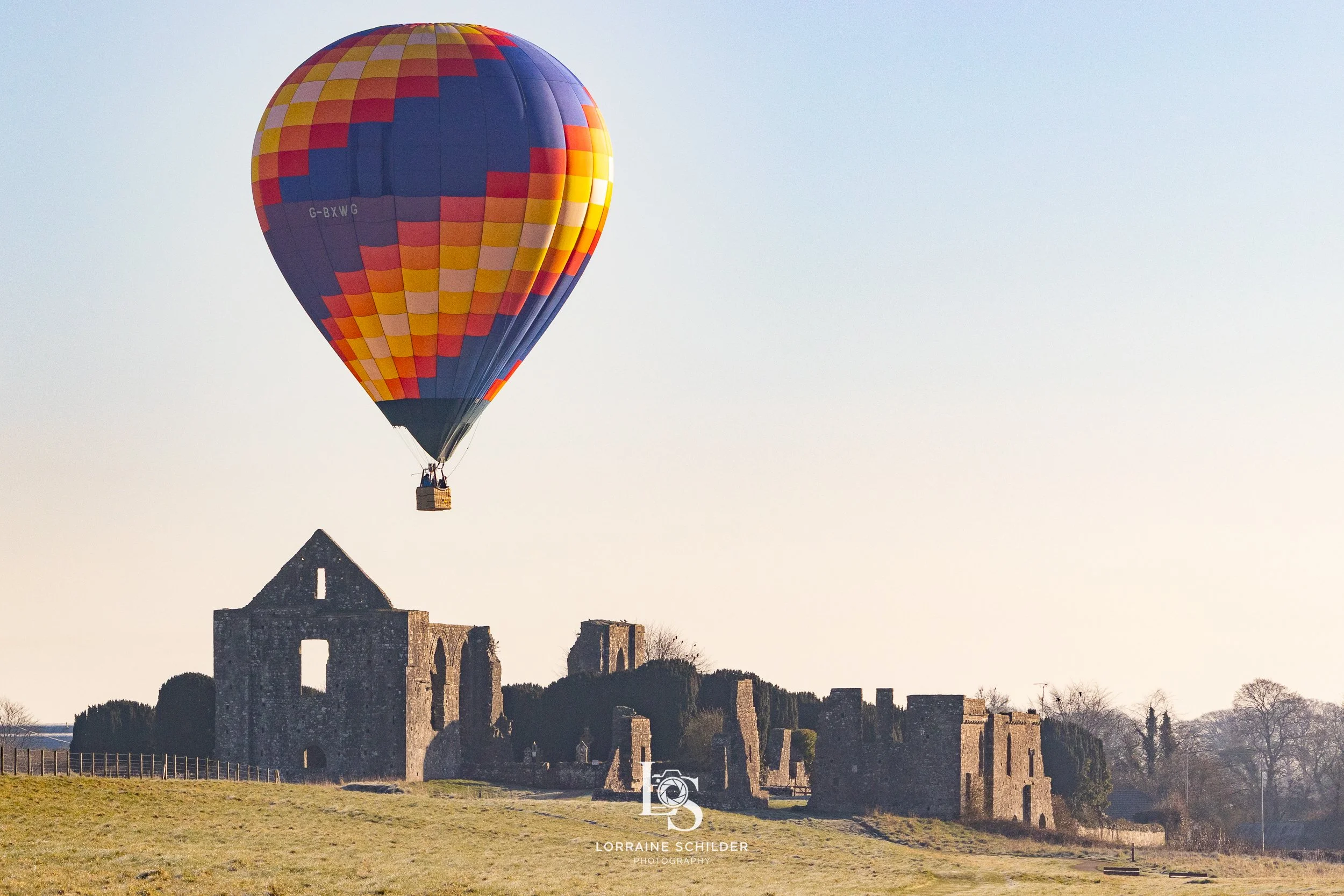 A colorful hot air balloon floating above the Newtown ruins in the grassy field during daylight.