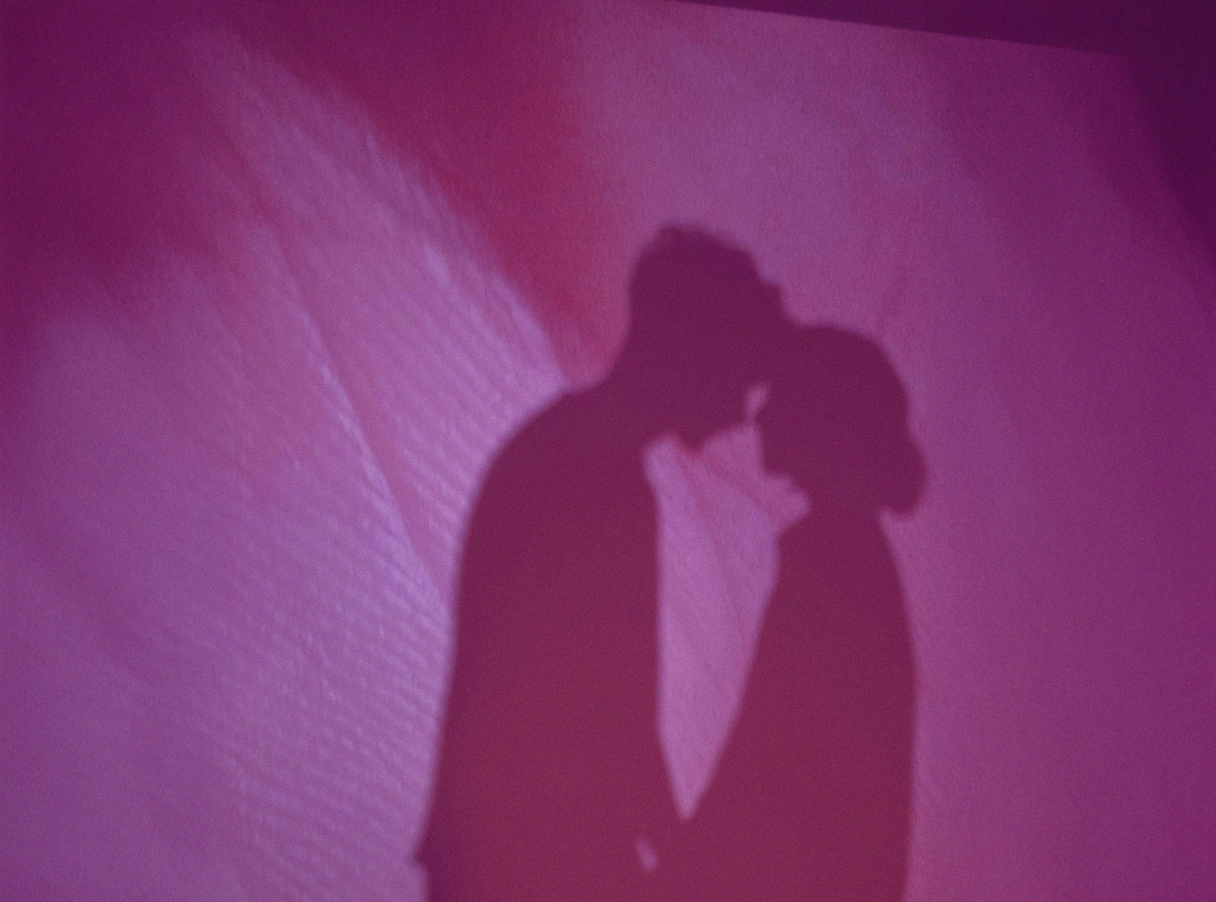 Shadow of a couple kissing projected onto a pink and purple wallpaper