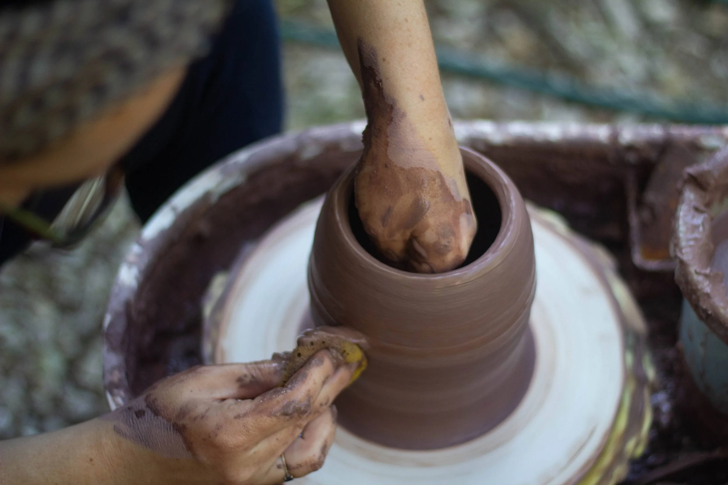 Une main mouillée façonne de la poterie en céramique humide sur un tour de potier, entouré d'argile et de matériaux de sculpture.