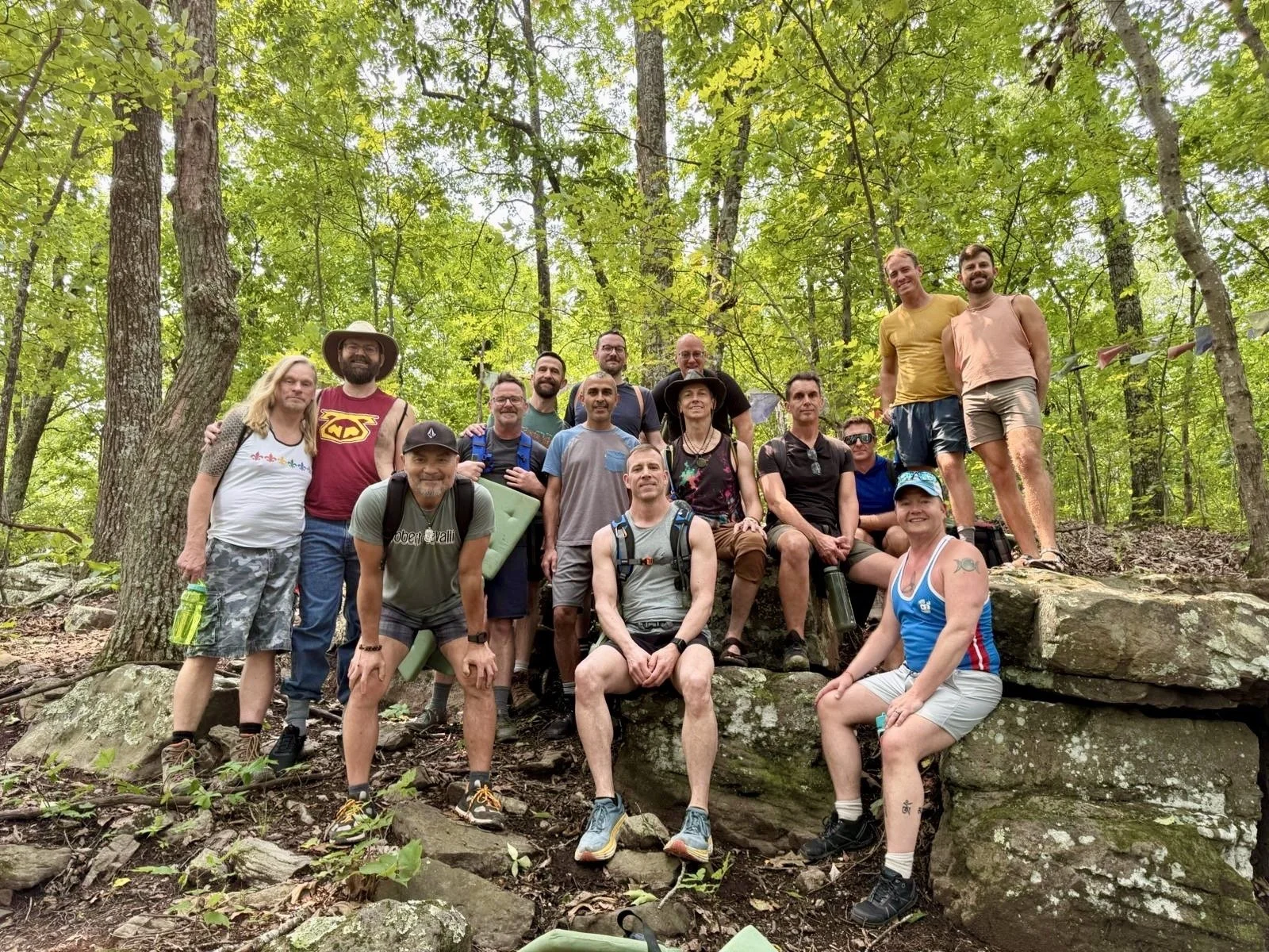 Group of people hiking in a forest, posing for a photo on rocks among trees with green leaves.