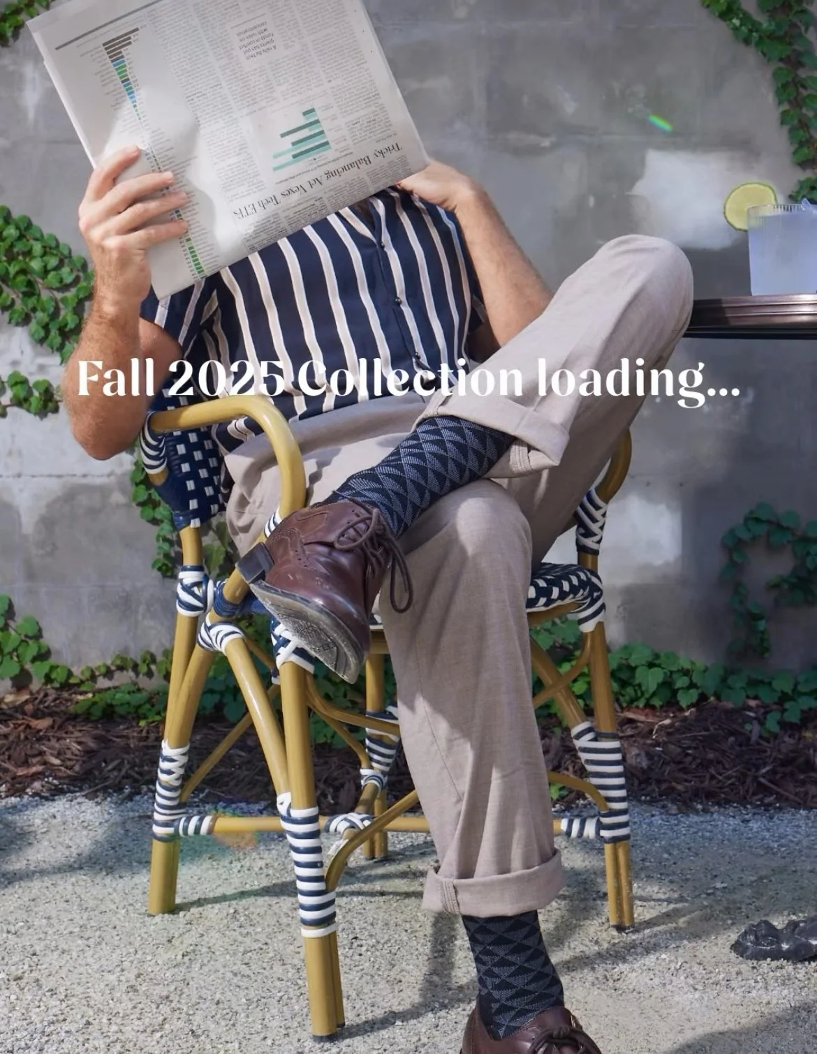 James sitting on cafe chair reading newspaper, with text overlay "Fall 2025 Collection loading...".