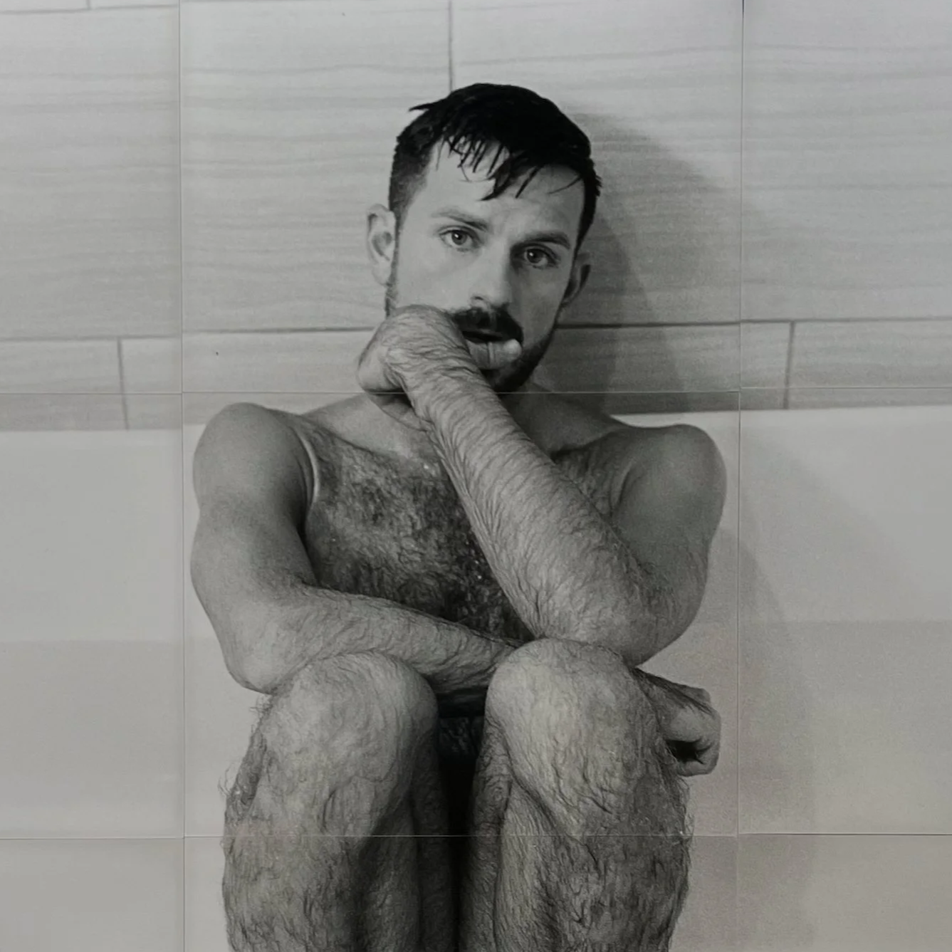 Black and white photo of James sitting in a bathtub with his knees pulled up, resting his chin on his hand, looking directly at the camera.