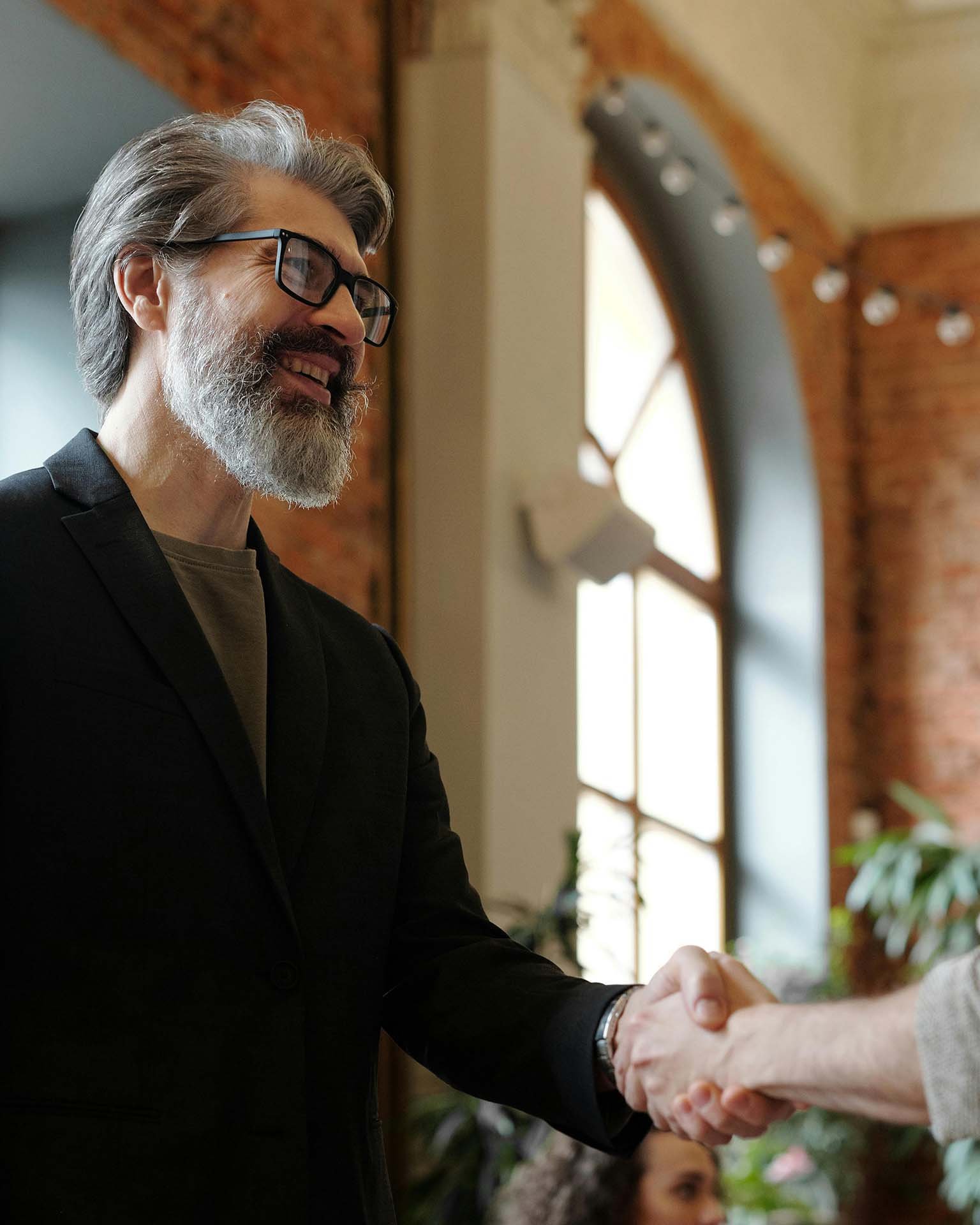 A professionally dressed business man shaking hands with another person in a business setting.