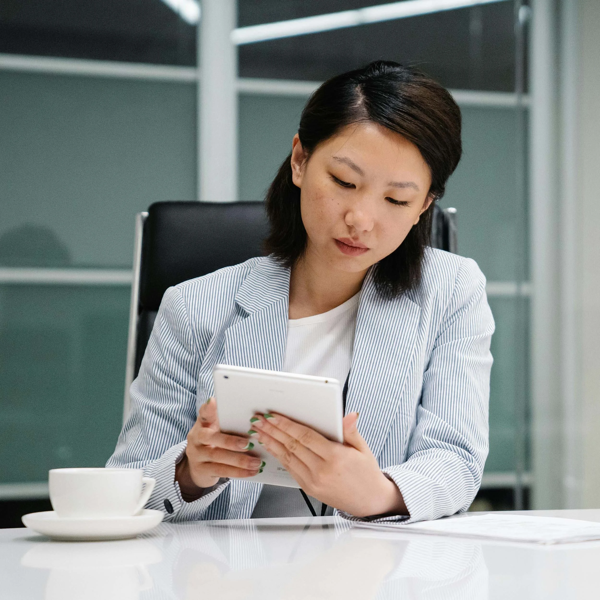 Asian woman looking at ipad with cup of coffee in office.jpg