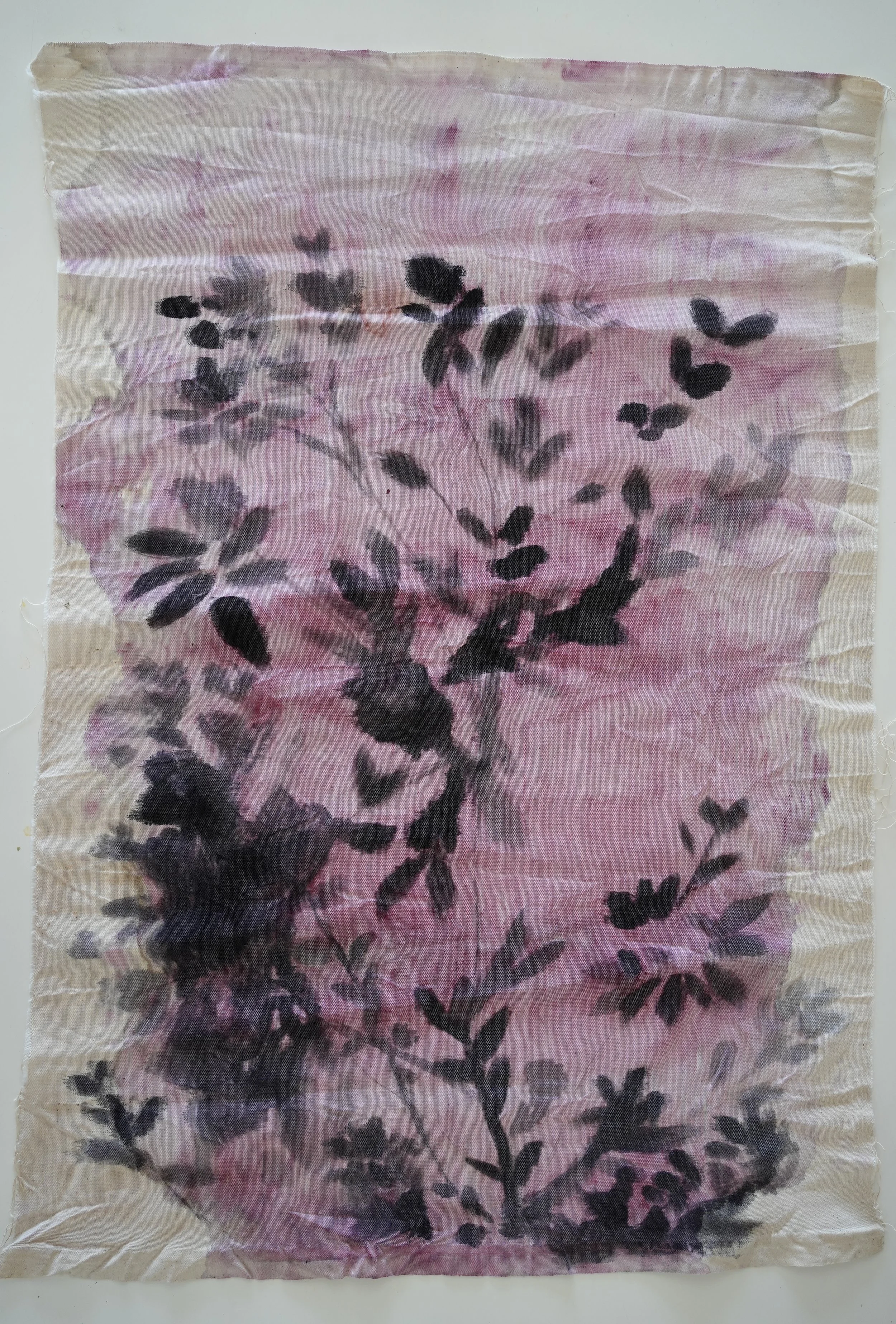 A crumpled piece of fabric with black ink botanical print on a pink and beige background.