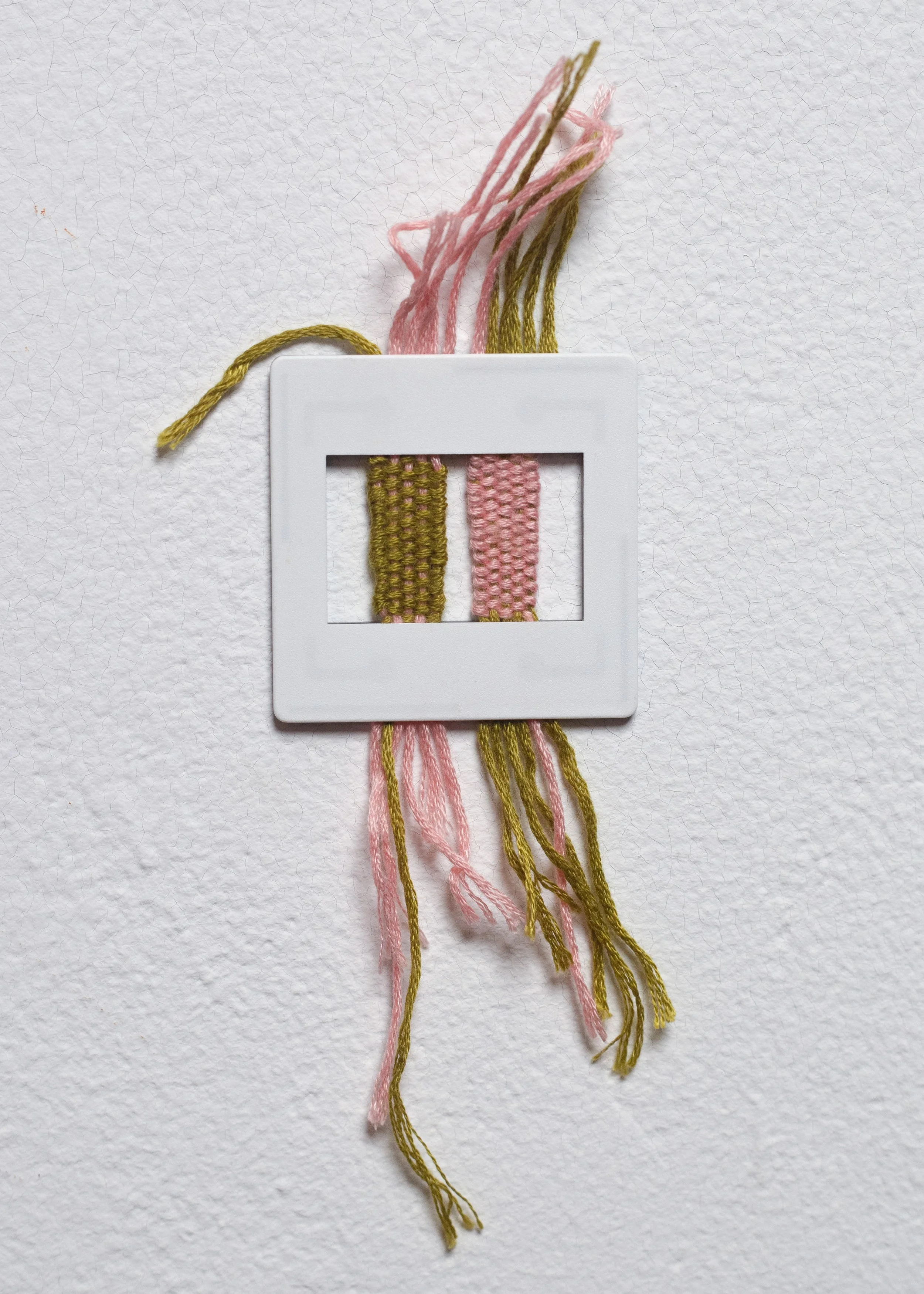 Close-up of embroidered threads in pink and green colors on a white background with a white plastic embroidery frame.