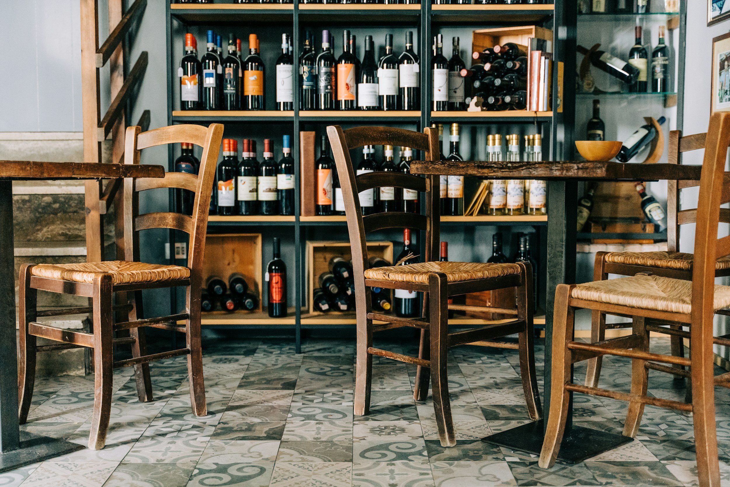 Interior of a wine shop or restaurant with wooden tables and chairs, and shelves filled with bottles of wine and wine accessories.