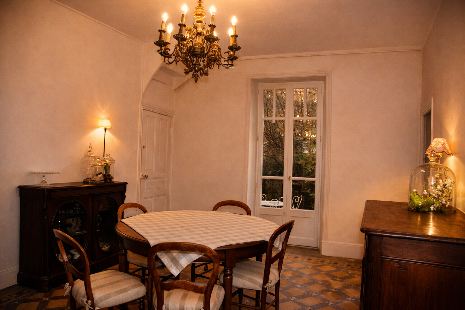 Elegant dining room with a chandelier, wooden table with a checkered tablecloth, four wooden chairs, a sideboard with glassware, and a large window showing trees outside.