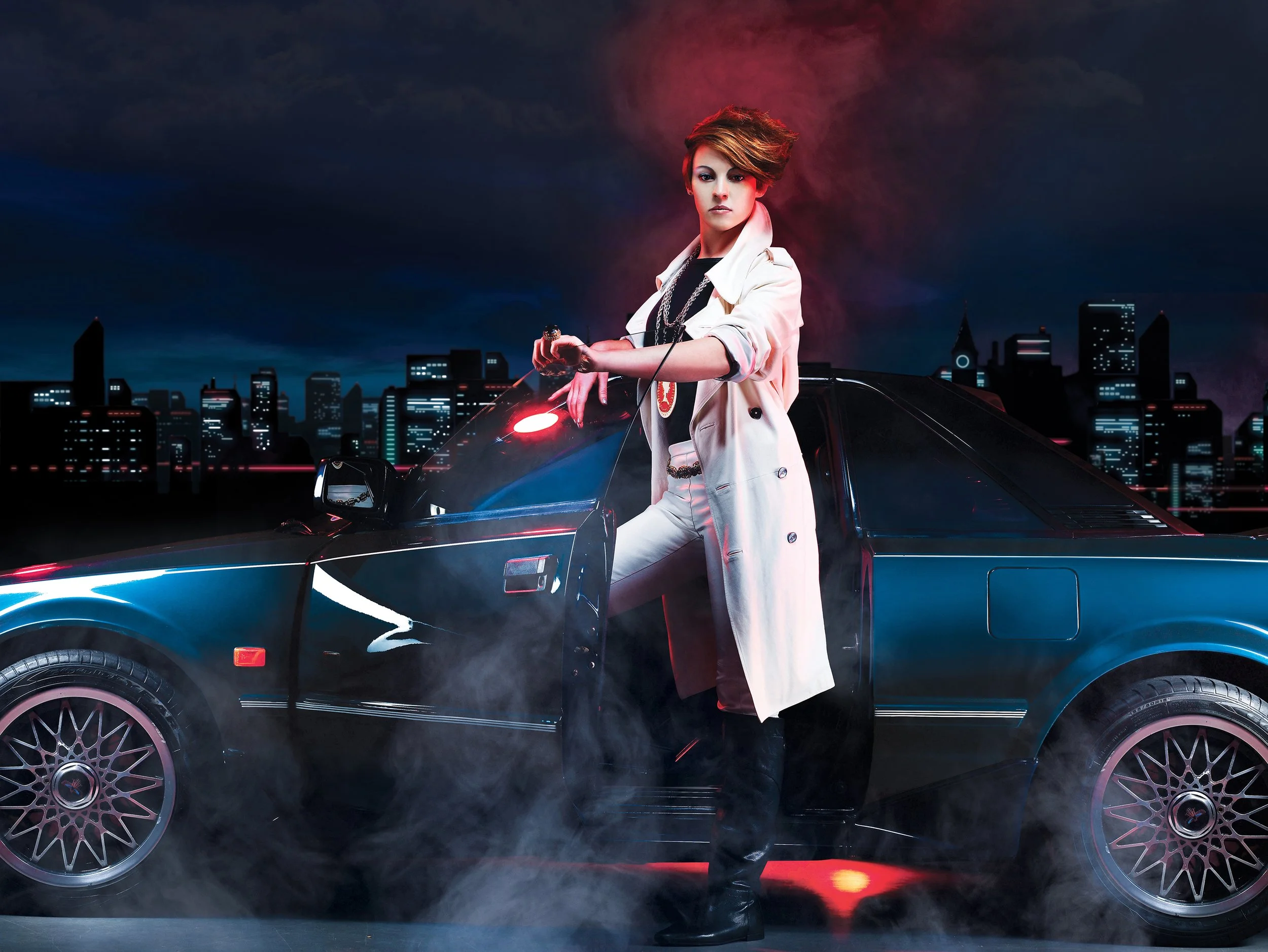 La Roux in white trench coat leaning on a black sports car with city skyline and dark cloudy sky in the background, smoke on the ground, neon lights illuminating the scene. Image used for her song 'In For the Kill'