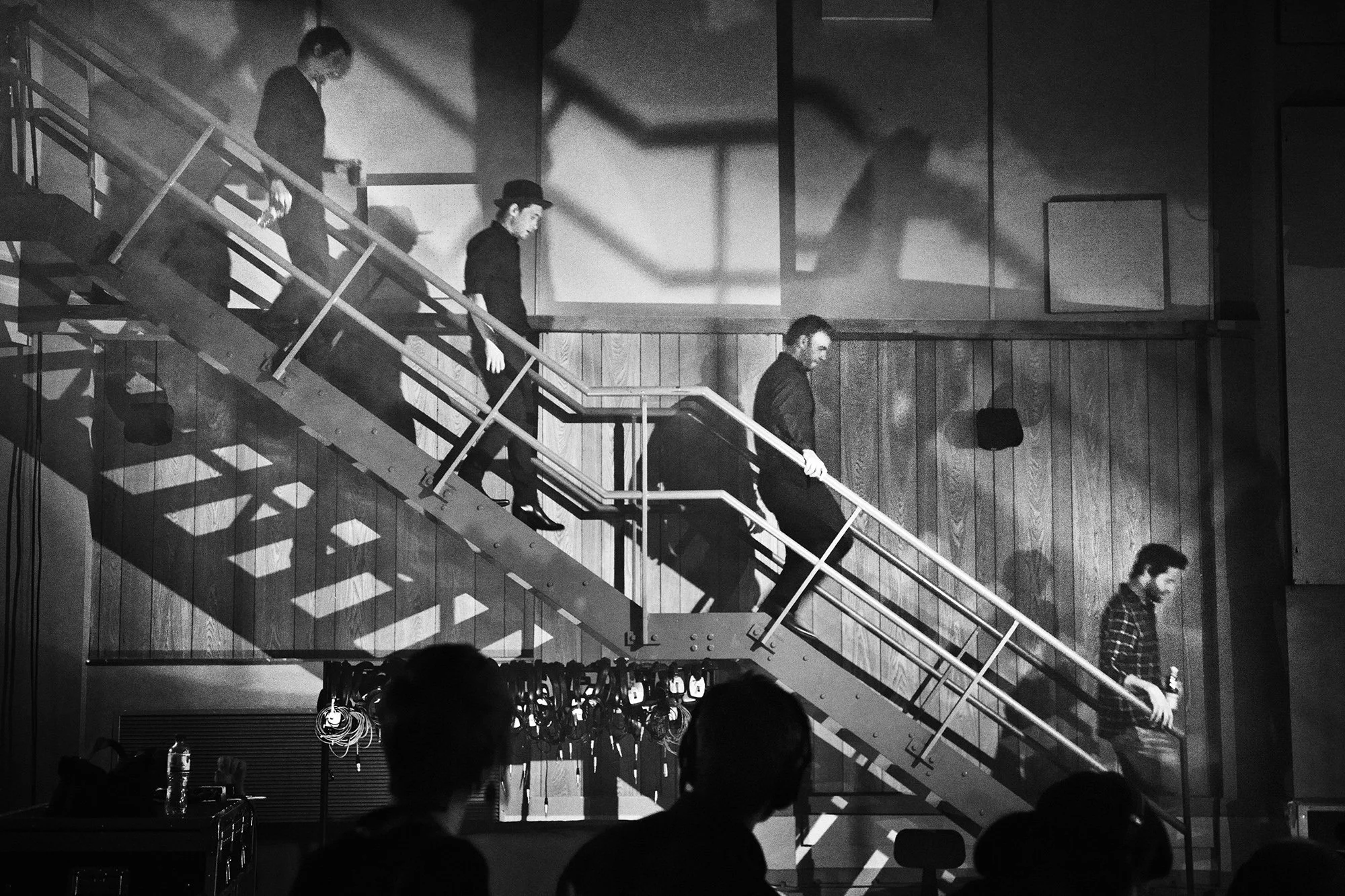 Take That walking down a staircase in an indoor setting, with shadows cast on the wall behind them and people in the foreground.