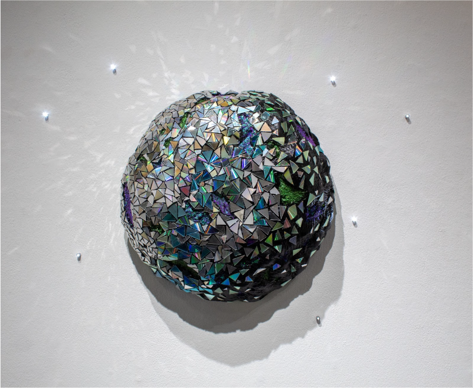 Amanda Chapman
Disco Meteorite, 2025
CDs, and glitter

Amanda Chapman explores emphasis on size, her imagination, and materials new to her with this holographic piece titled ‘Disco Meteorite.’ She is inspired by her love of bright colors, light inter