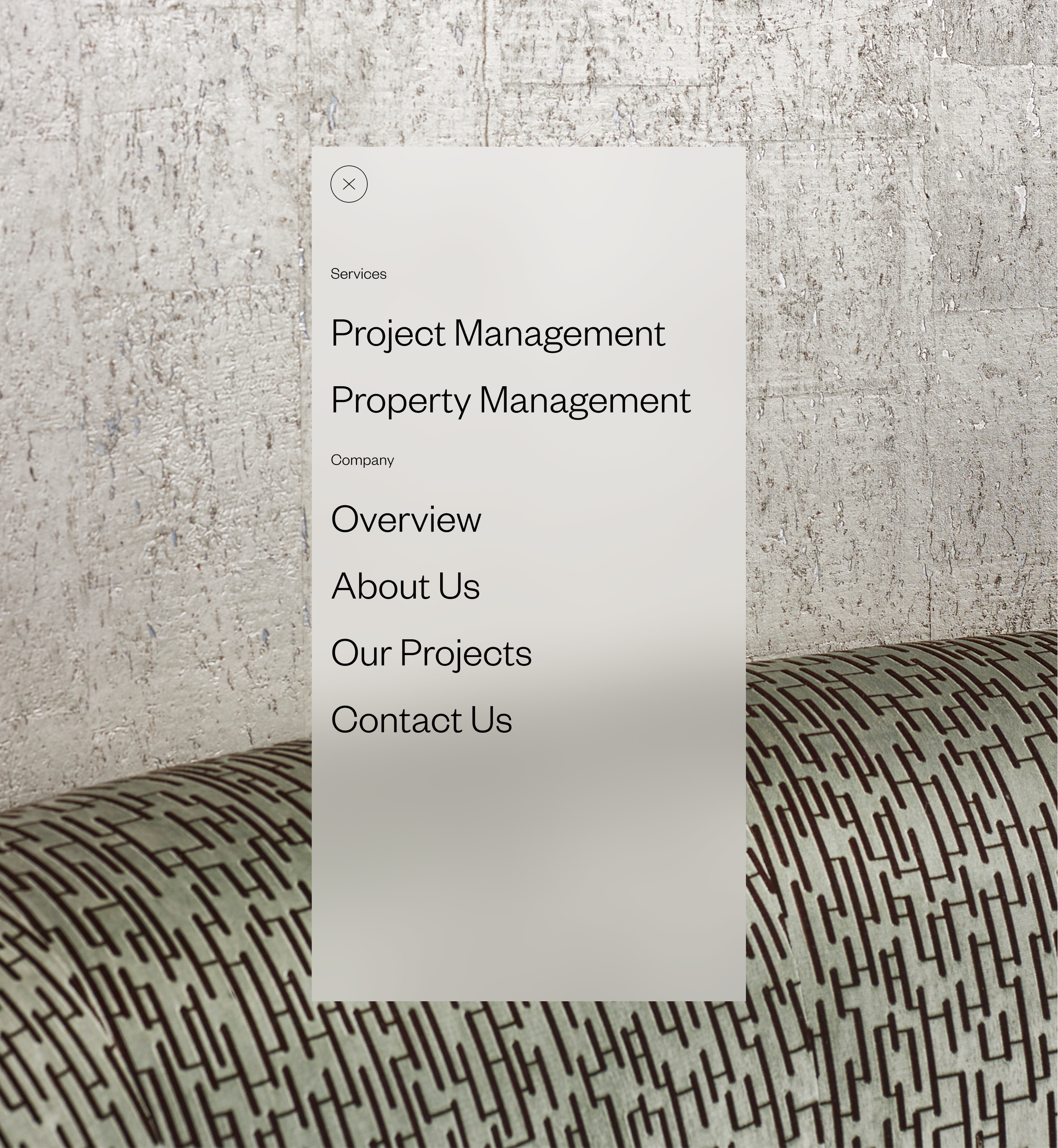 A mobile device displaying a menu for services including project management and property management, over a textured wall and patterned furniture.