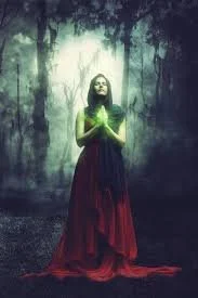 A woman in a red dress standing in a misty forest with glowing light behind her, holding her hands together in front of her chest.