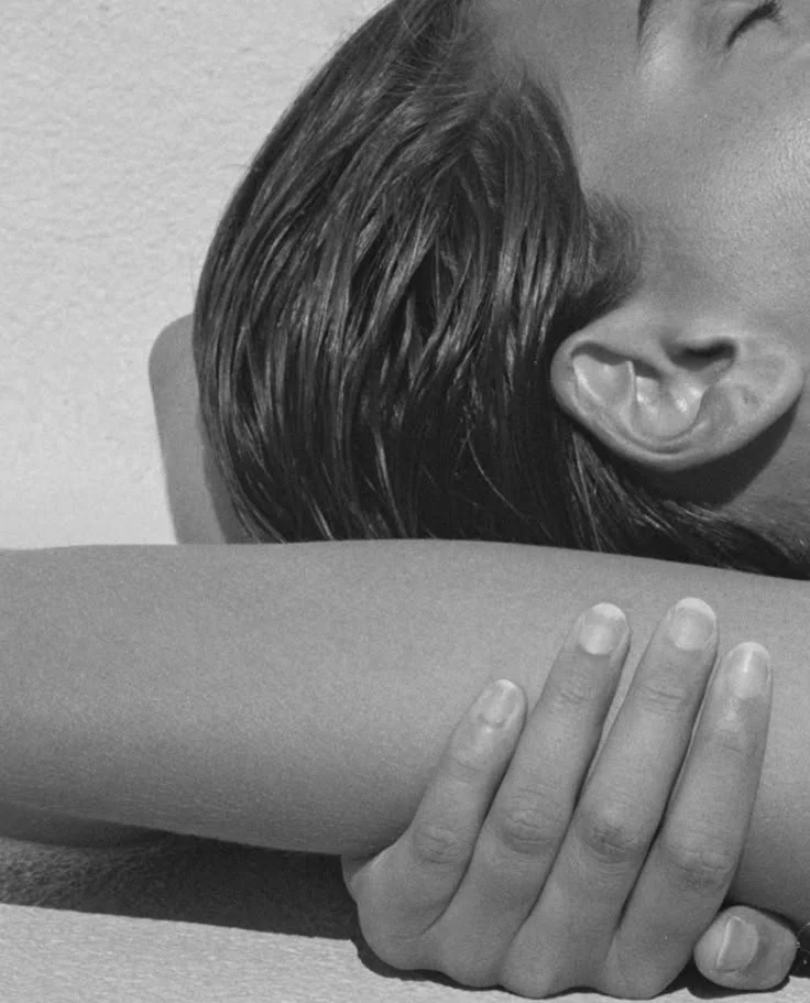 Close-up black and white photo of a person's face partially visible, resting on a person's arm, with fingers grasping the arm.