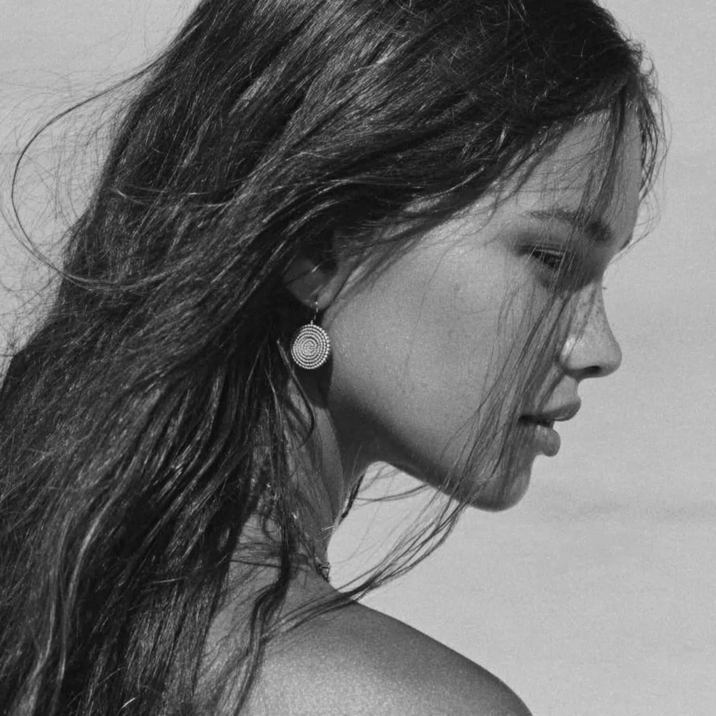 A black and white close-up side profile of a woman with long, wavy hair, wearing spiral-shaped earrings.