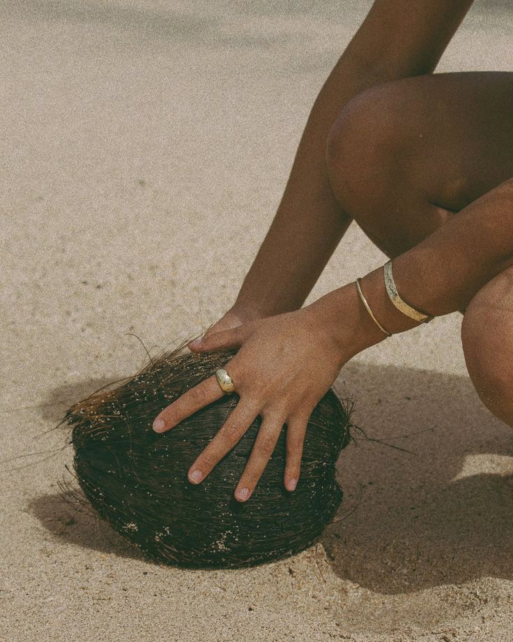 Person with multiple rings on hand, touching a large black sea urchin on sandy beach.