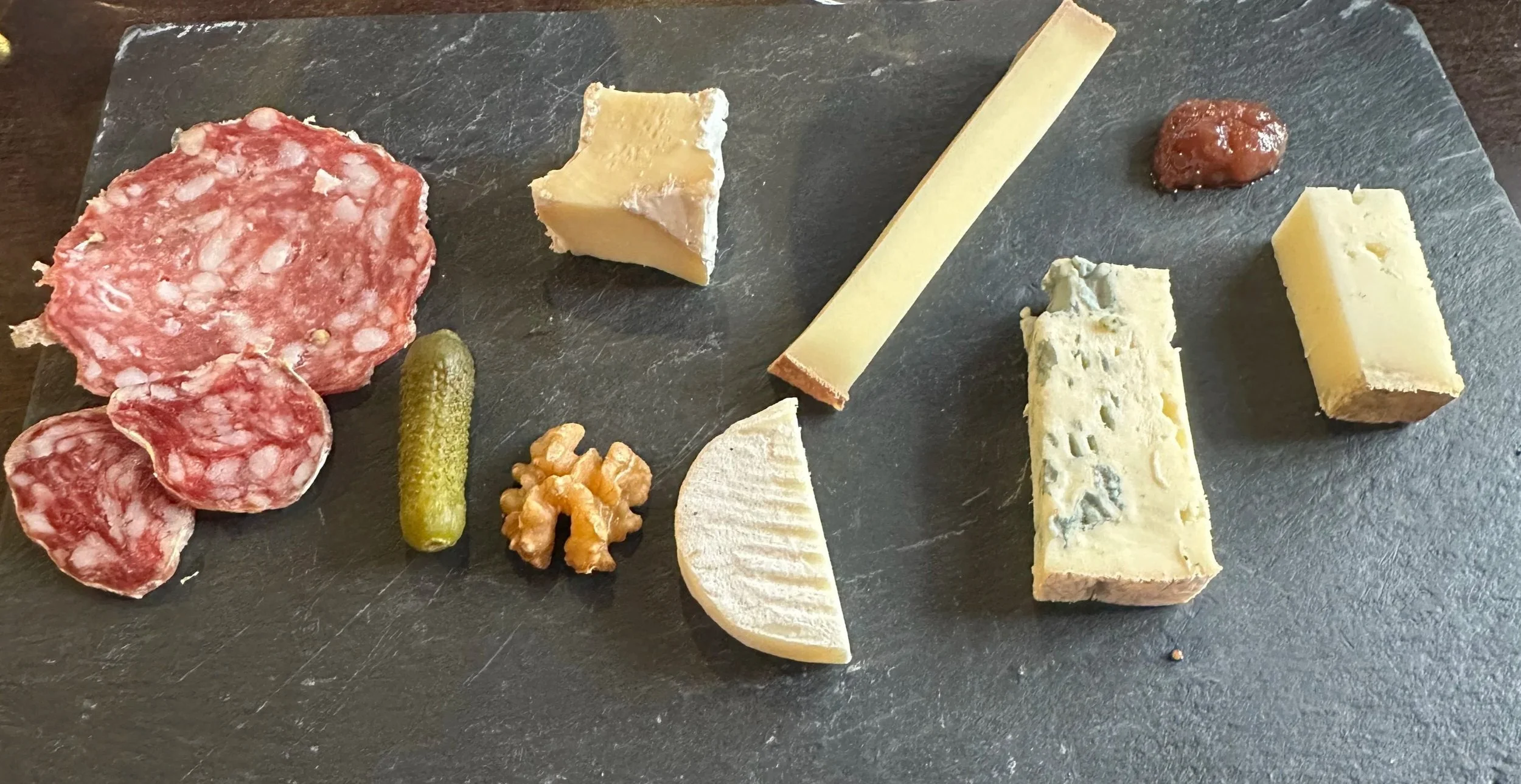 Assorted cheeses, cured meats, and accompaniments on a dark slate serving board.