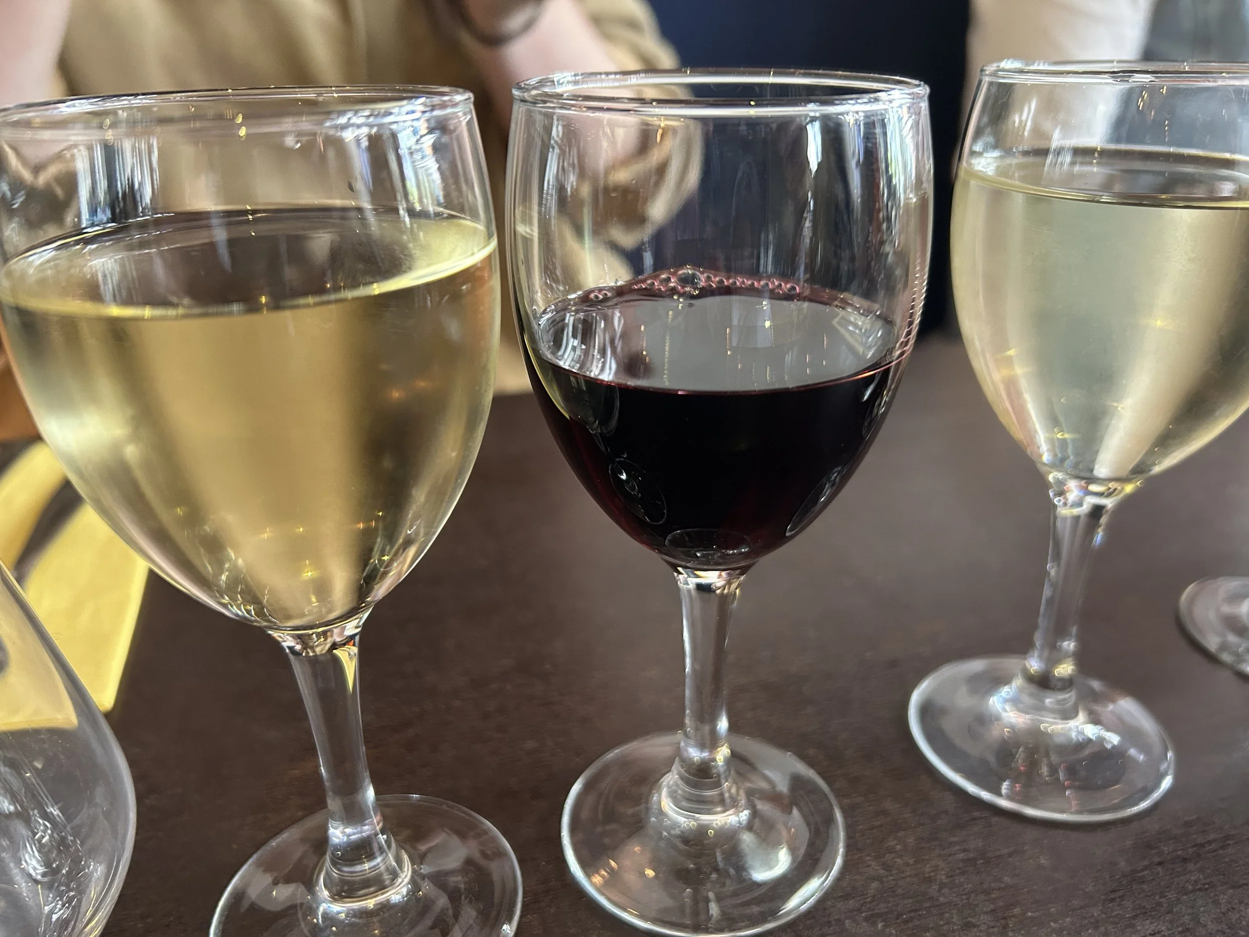 Three wine glasses on a table, two with white wine, one with red wine.