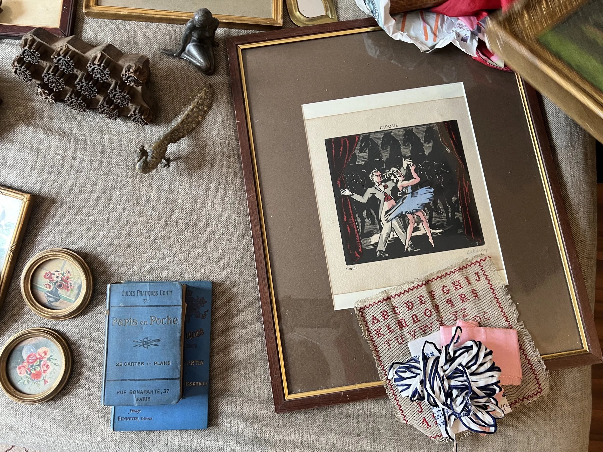 A collection of vintage items including framed artwork, small framed floral pictures, miniature books, and various trinkets on a textured surface.