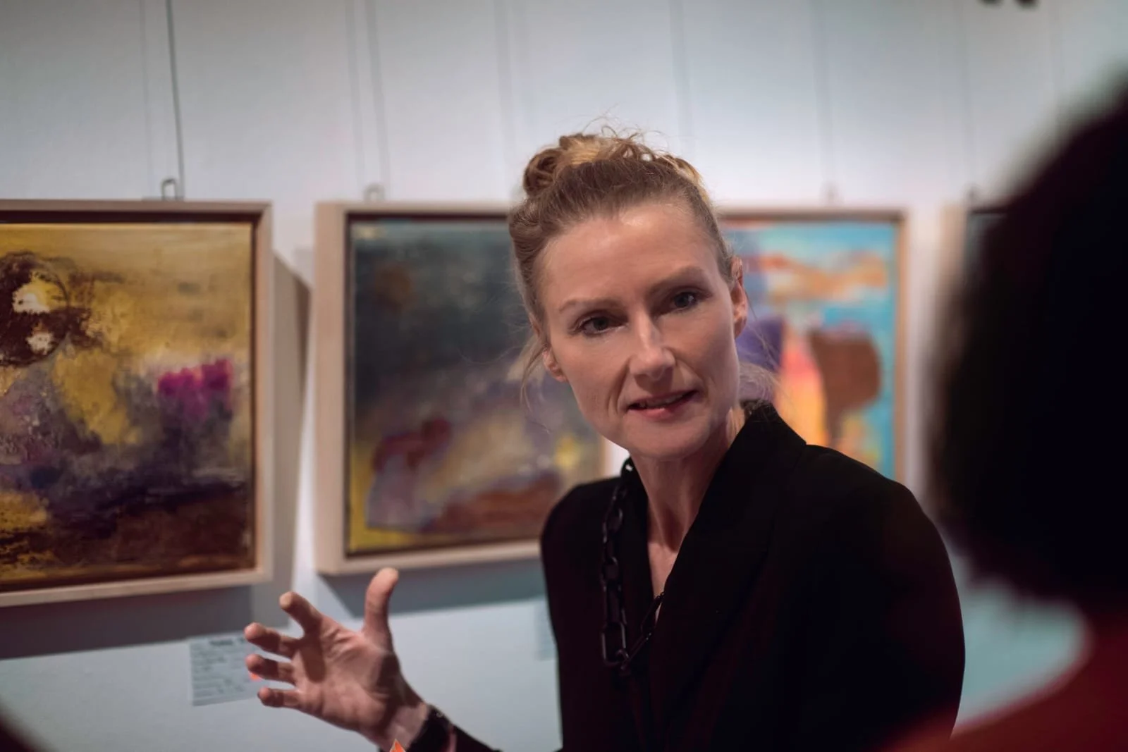Die Künstlerin Stefanie Rau in Nahaufnahme steht vor ihren abstrakten Kunstwerken auf der Vernissage und spricht mit Besuchern. 