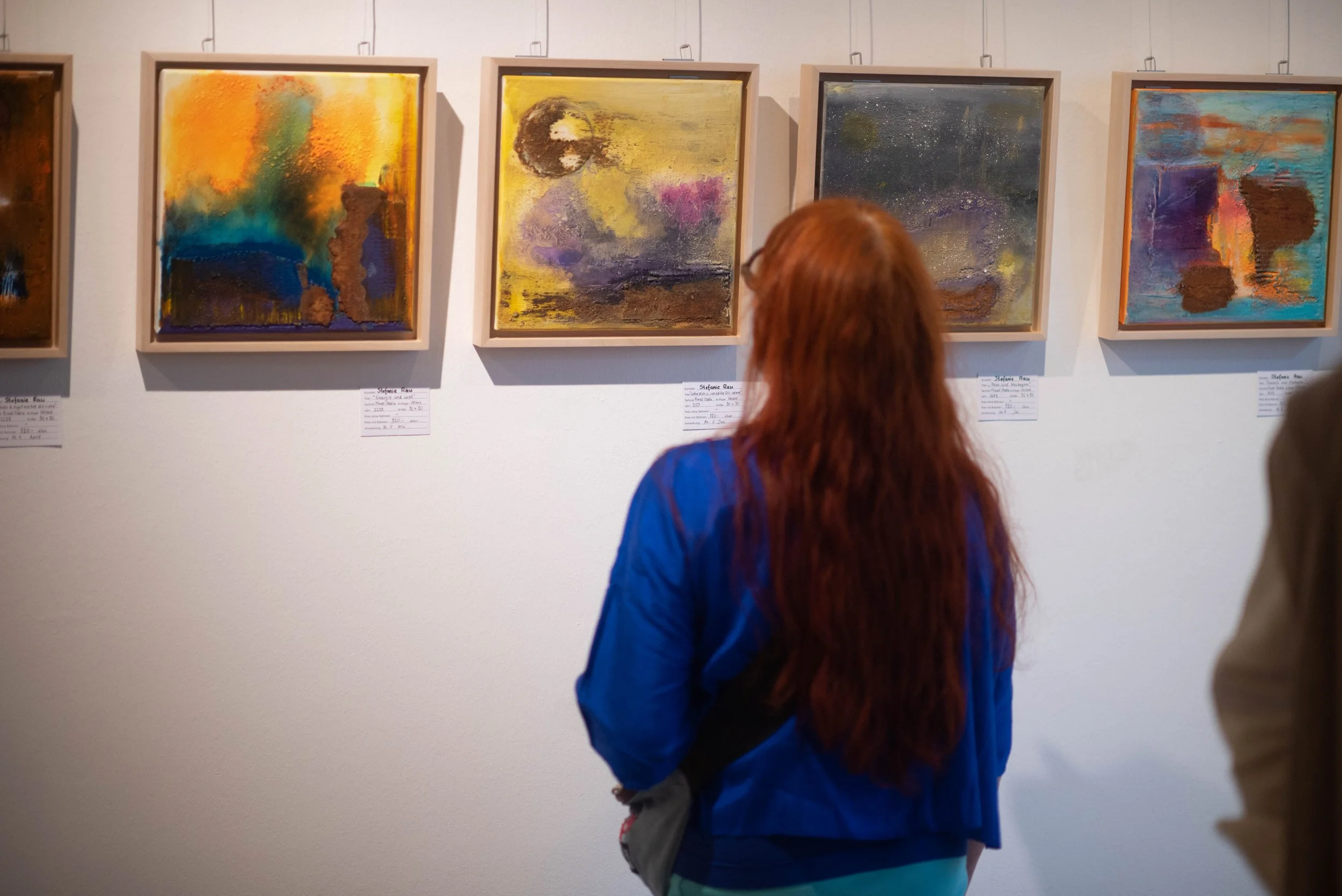 Eine Besucherin der Vernissage, die abstrakte Kunstwerke betrachtet.